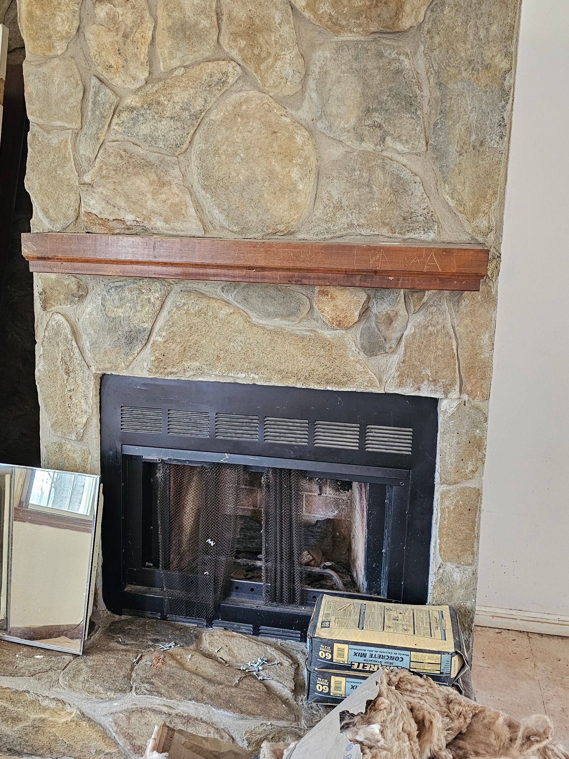 Stone fireplace with a black firebox and wooden mantel. Construction debris nearby.