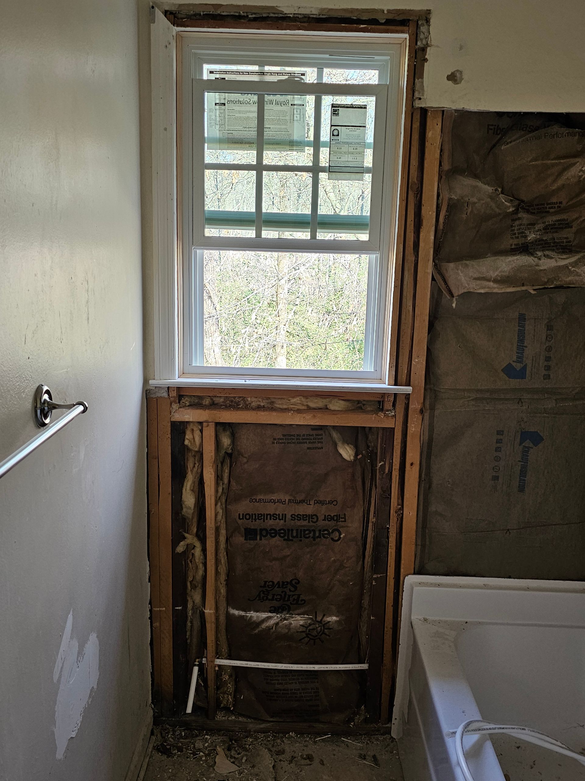 Bathroom wall with exposed framing around a window during renovation. Drywall removed, insulation visible.