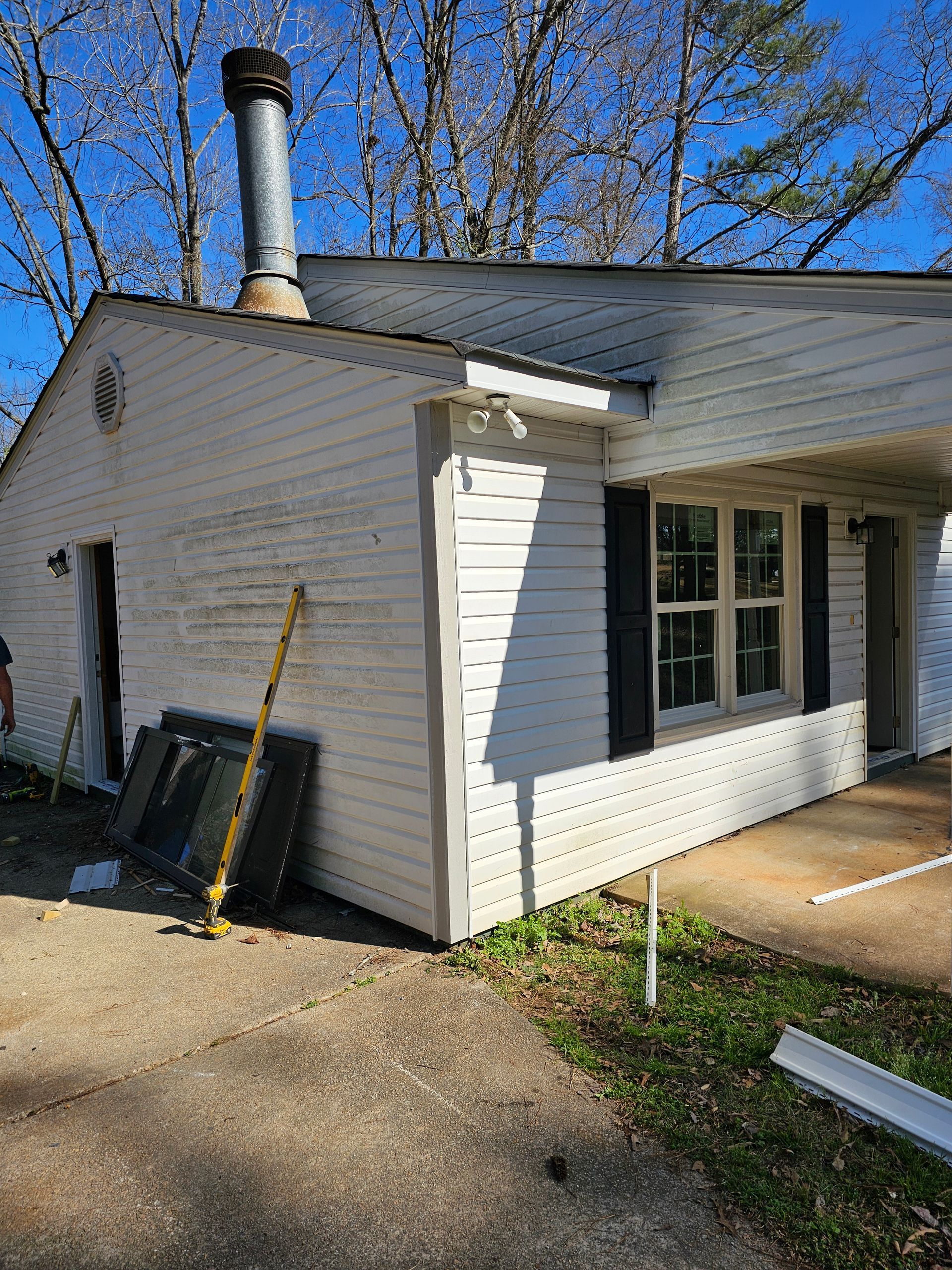 White house with peeling siding, chimney, carport, and shutters.