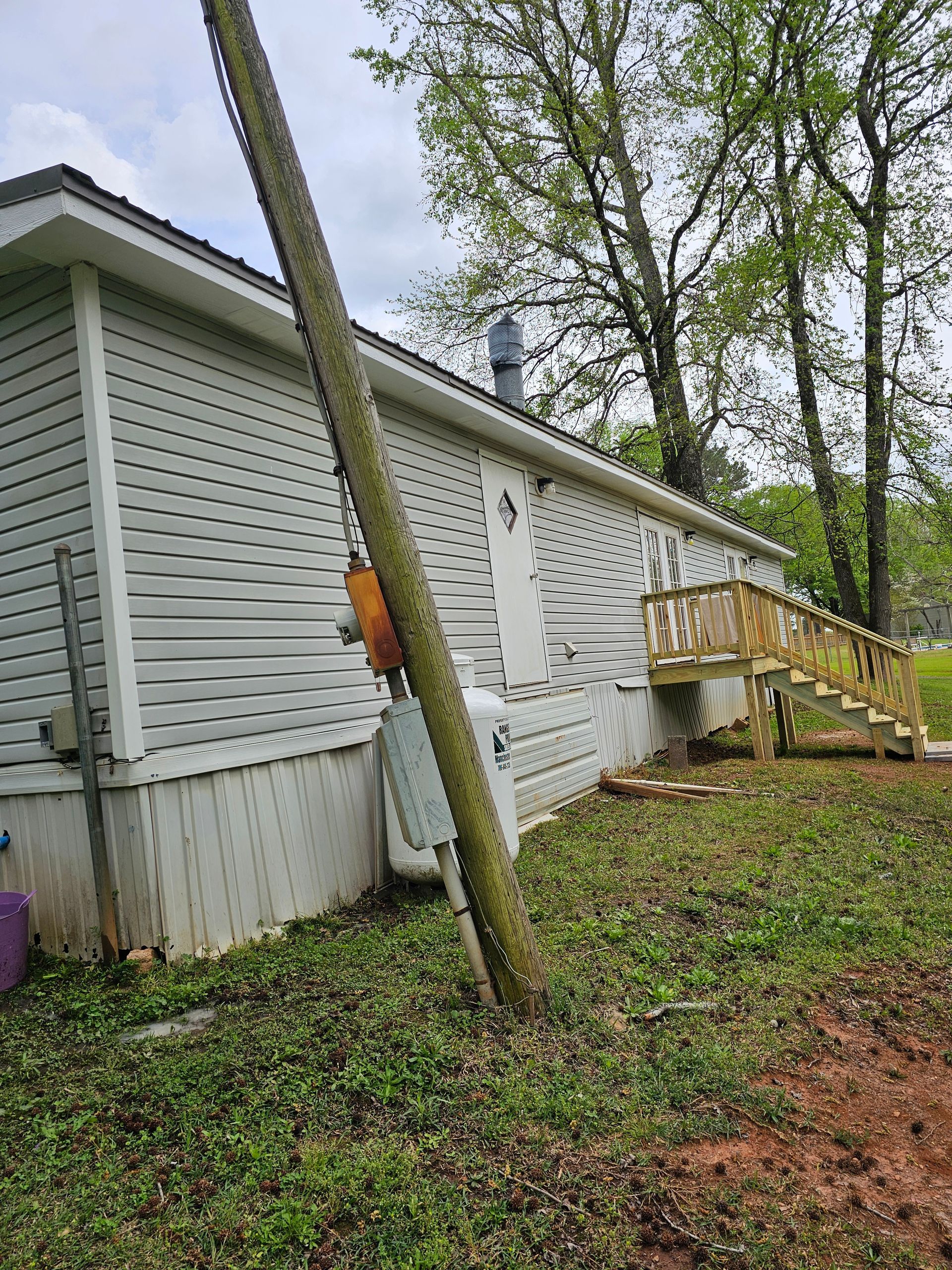 Side view of a light gray house with a wooden deck and utility pole in the yard.