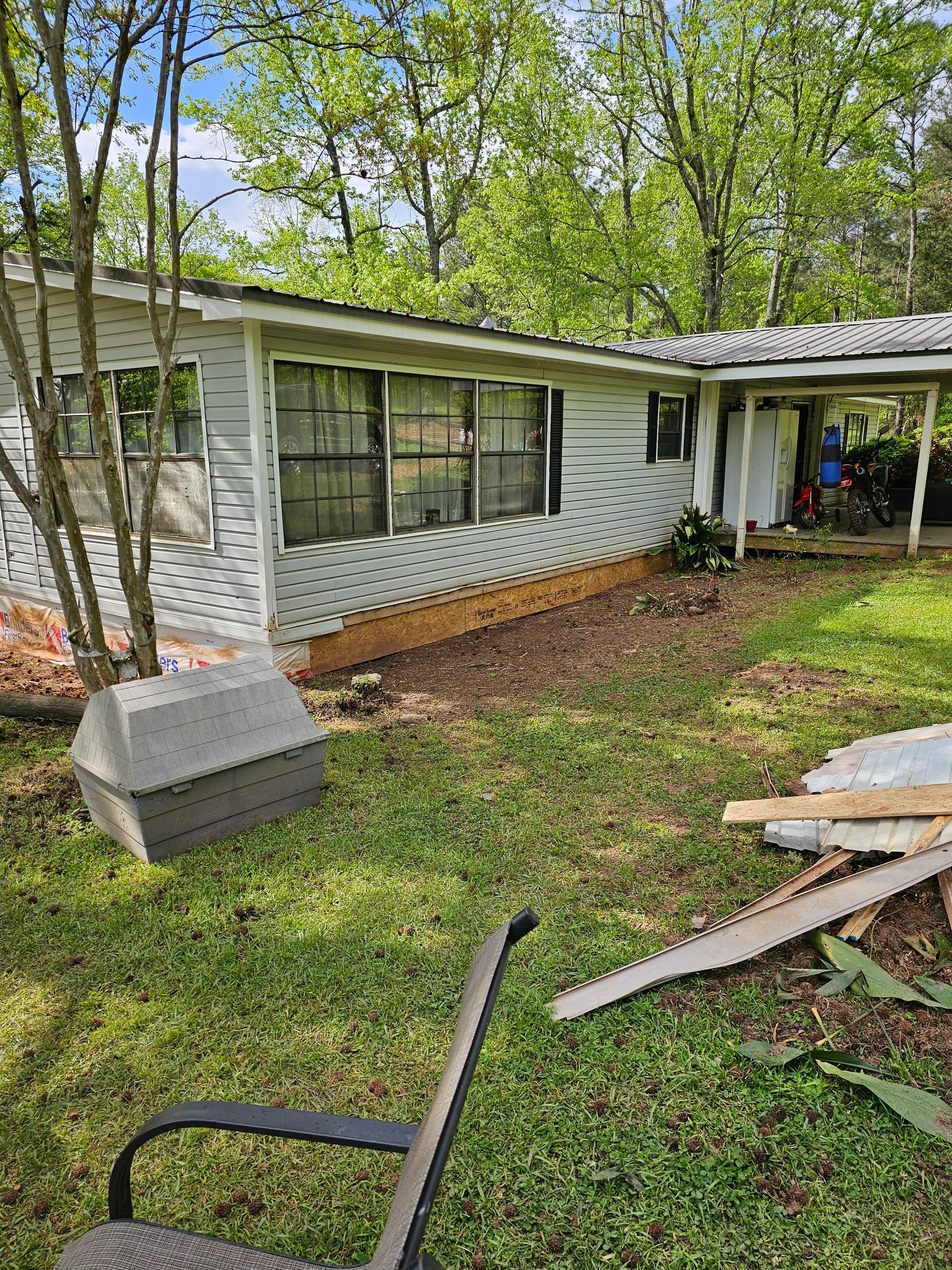 White house with windows, carport, and grassy yard with debris.