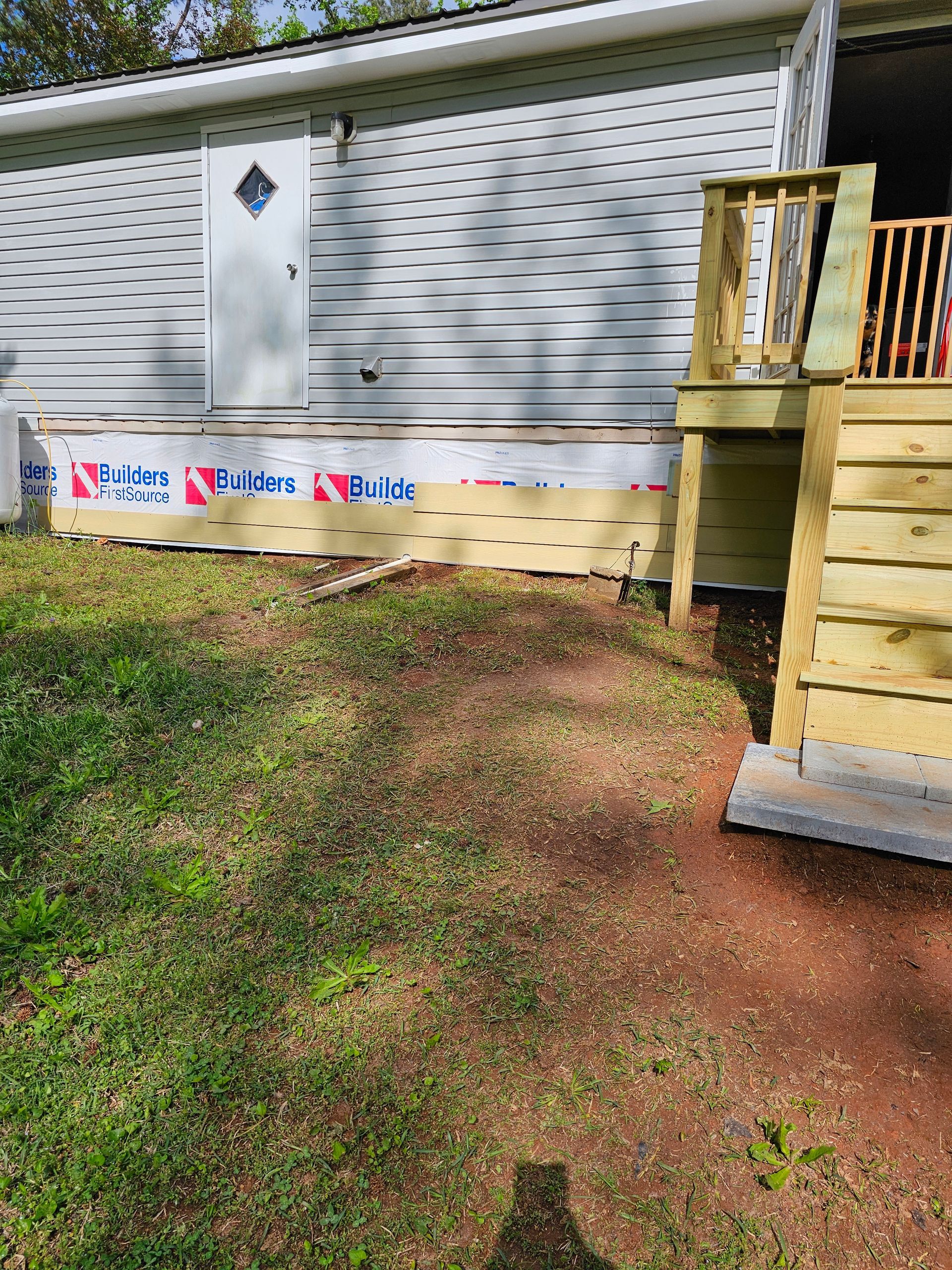 Mobile home exterior with exposed insulation, unfinished deck steps, and dirt yard.
