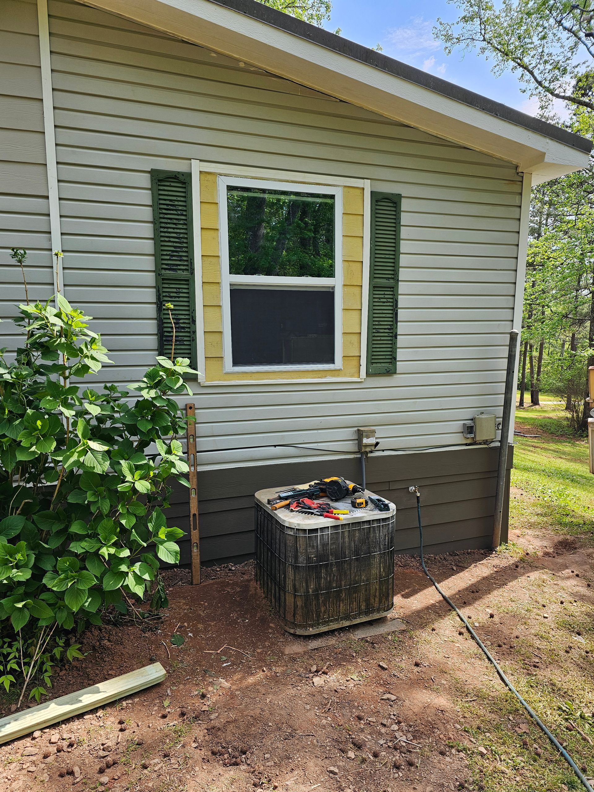 A house with gray siding, yellow window trim, green shutters, and an air conditioning unit.