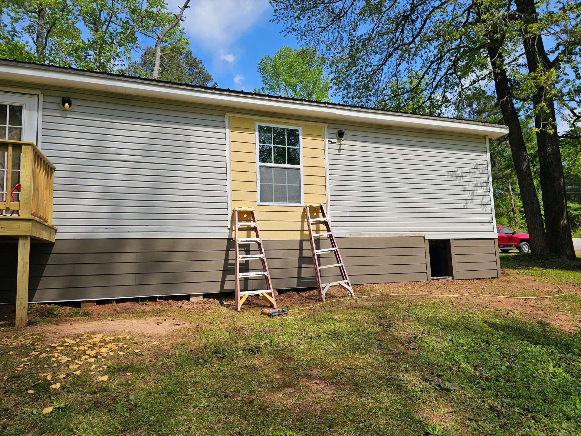 Exterior of a house under construction. A door frame is painted yellow, with two ladders. Grey siding and brown foundation.