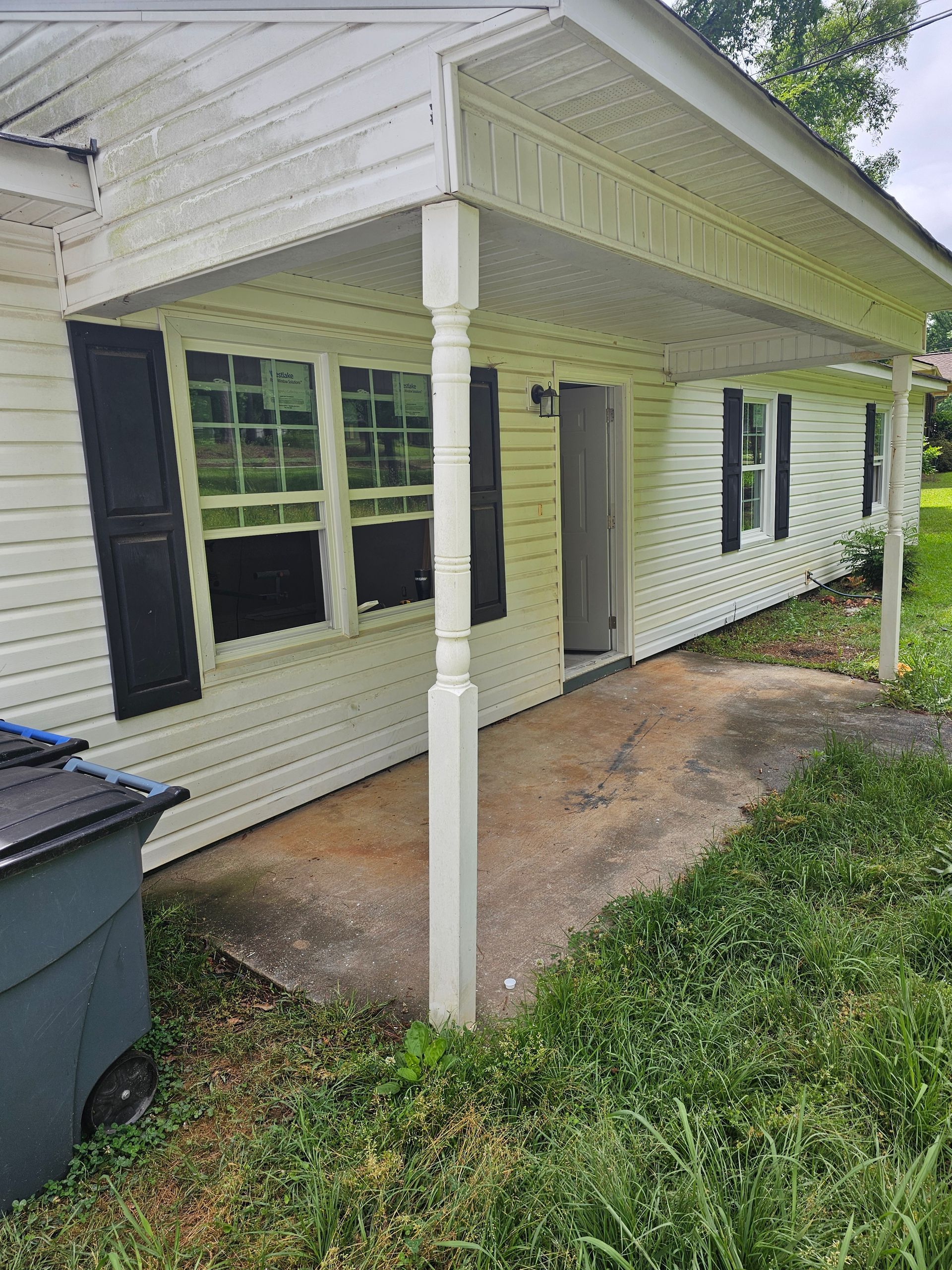 Exterior view of a white house with a porch. A front door is open. Black shutters and green grass are visible.
