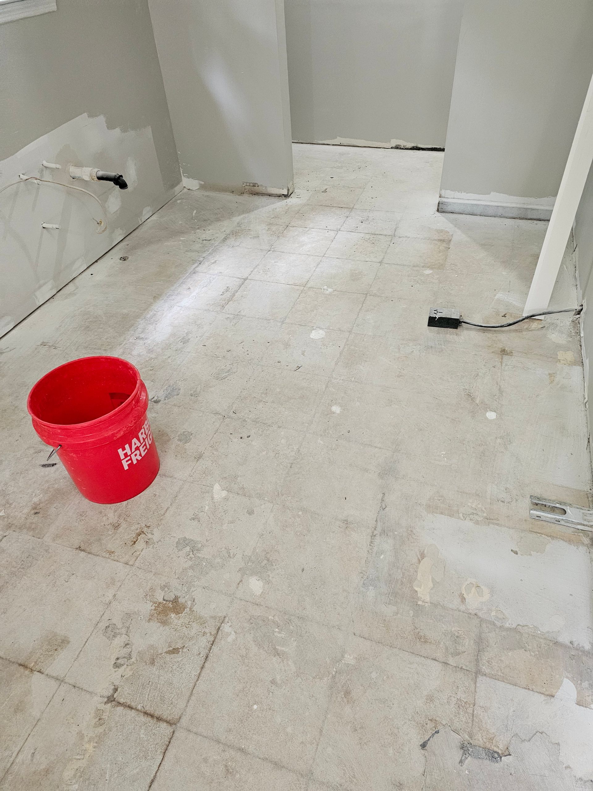 Room with concrete floor, red bucket. Walls are light gray, in a space under construction.