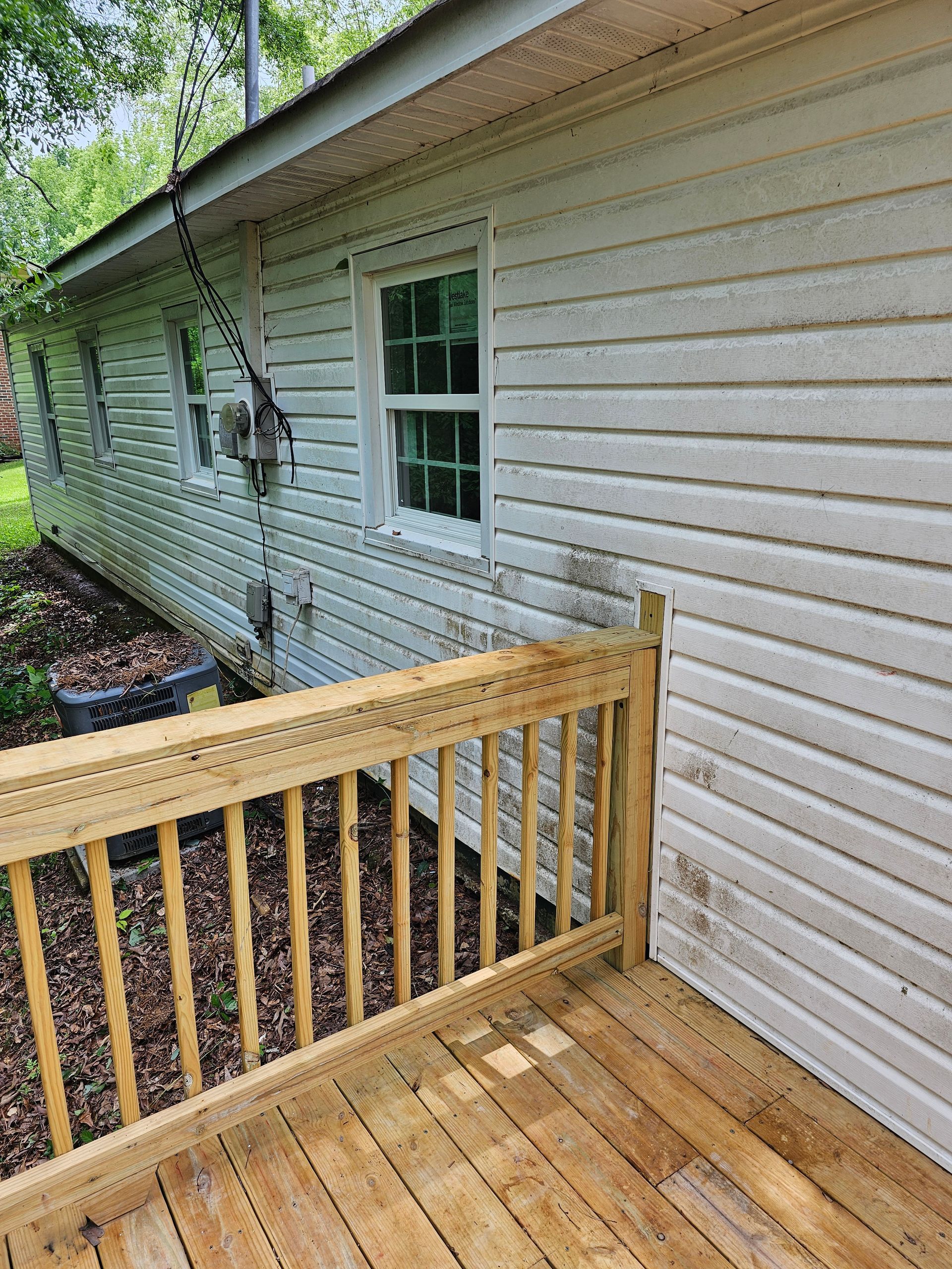 Wooden deck with railing next to a house with white siding and windows.
