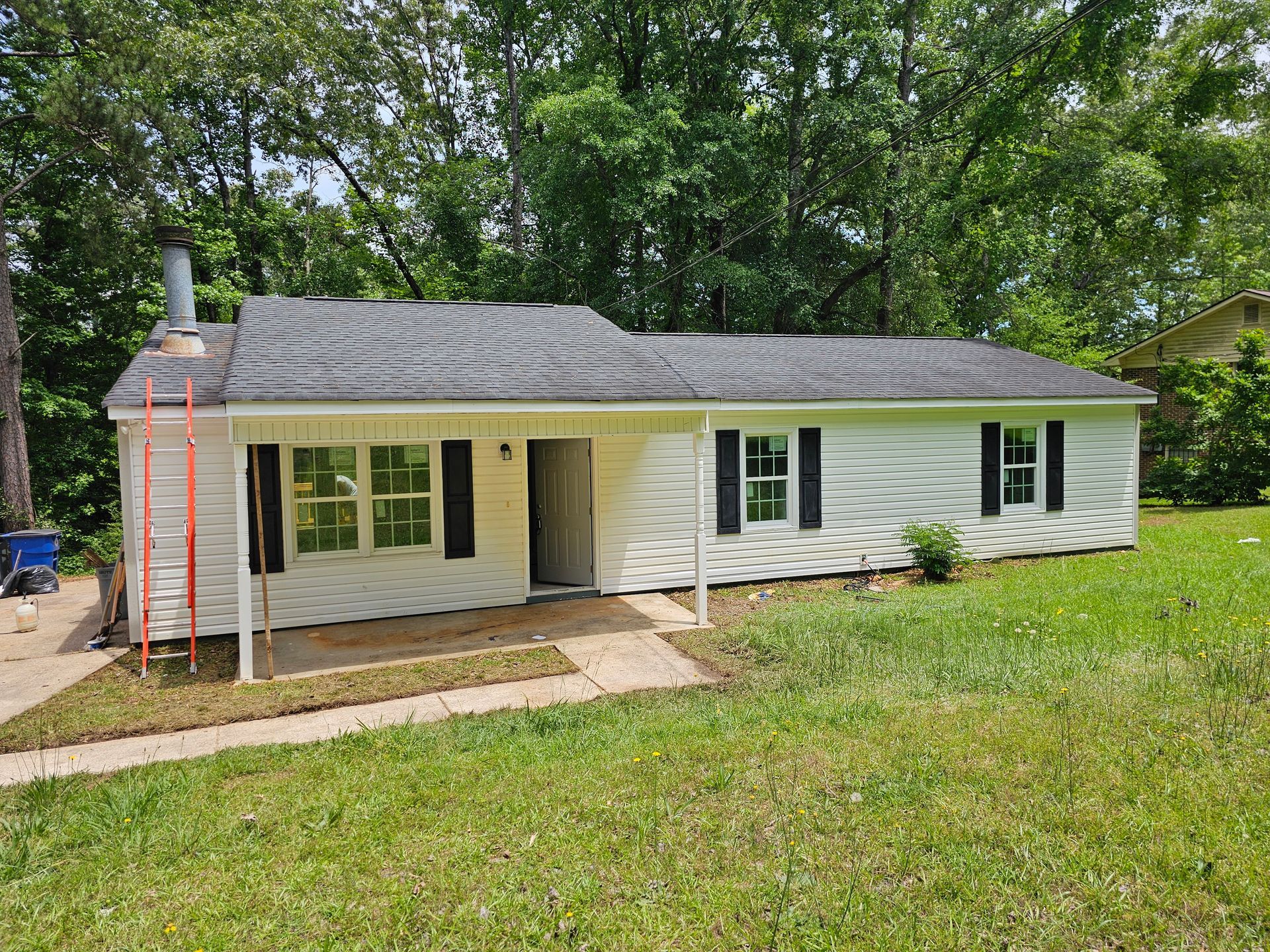 White, one-story house with black shutters, chimney, and a small front porch, set in grassy yard.