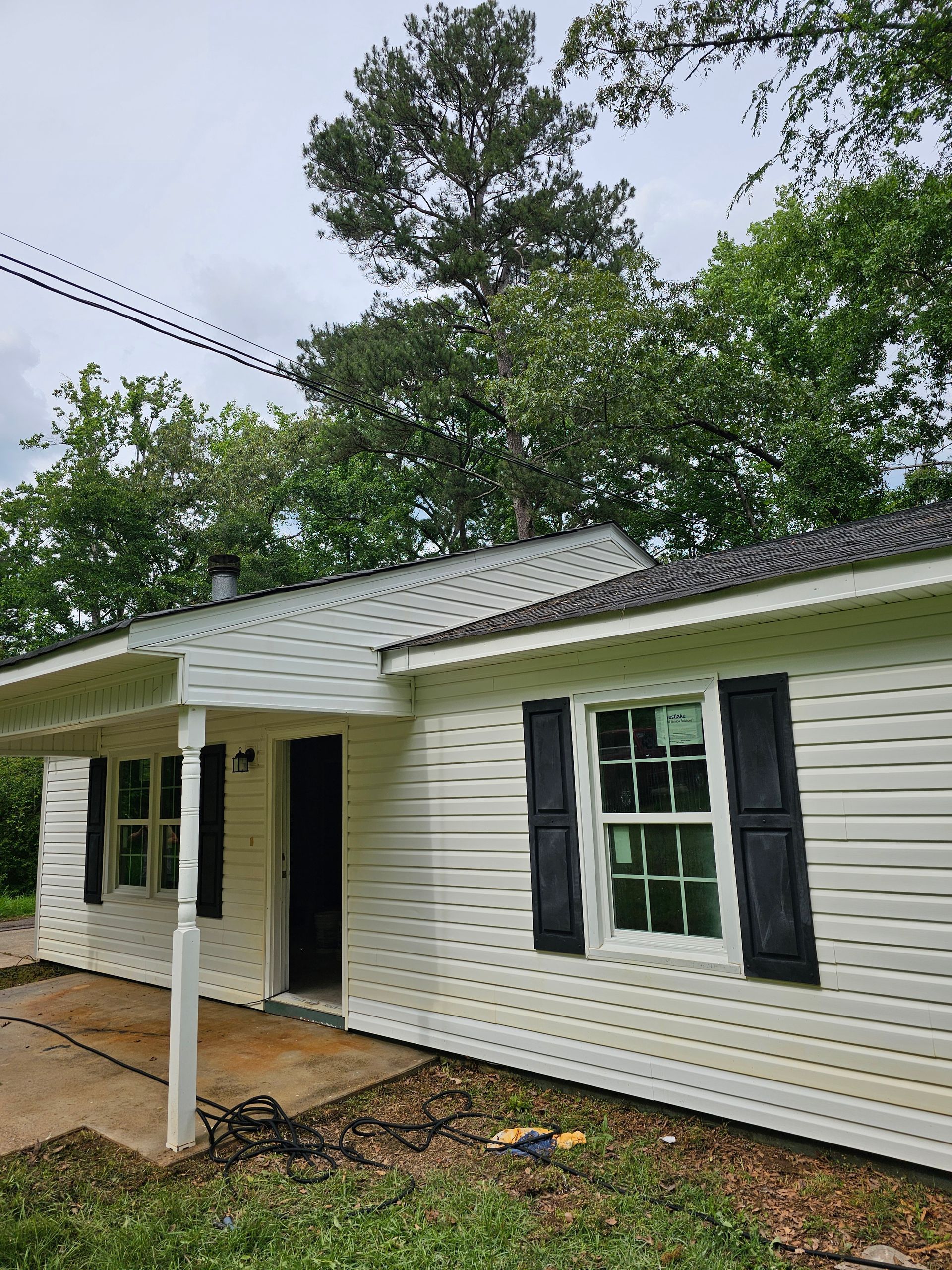 White house with black shutters, trees in background, cloudy sky.