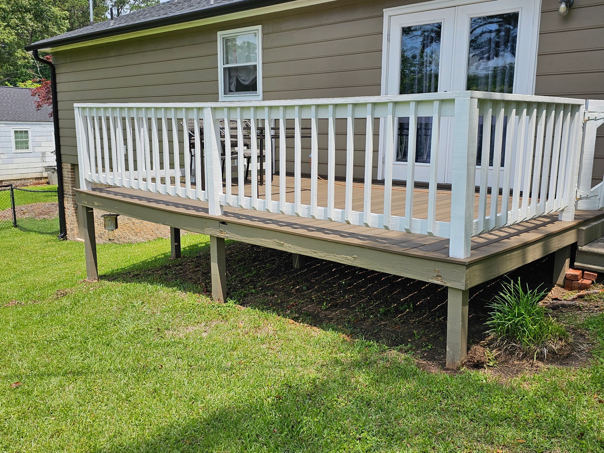 Wooden deck with white railing attached to a beige house, over green grass.