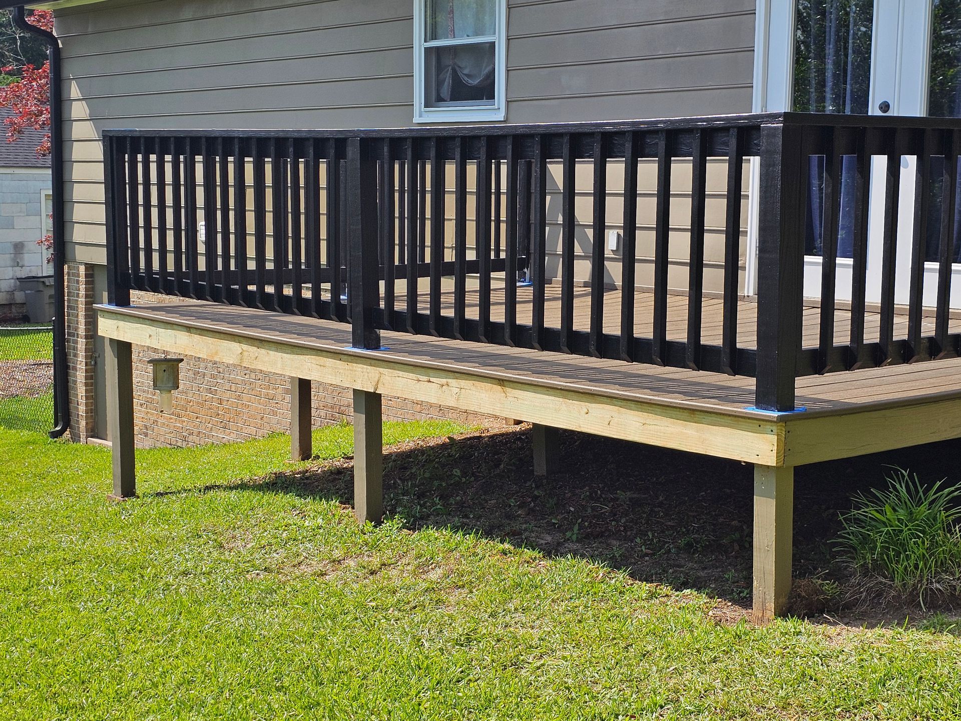 Wooden deck with black railing next to a house, on a grassy lawn.