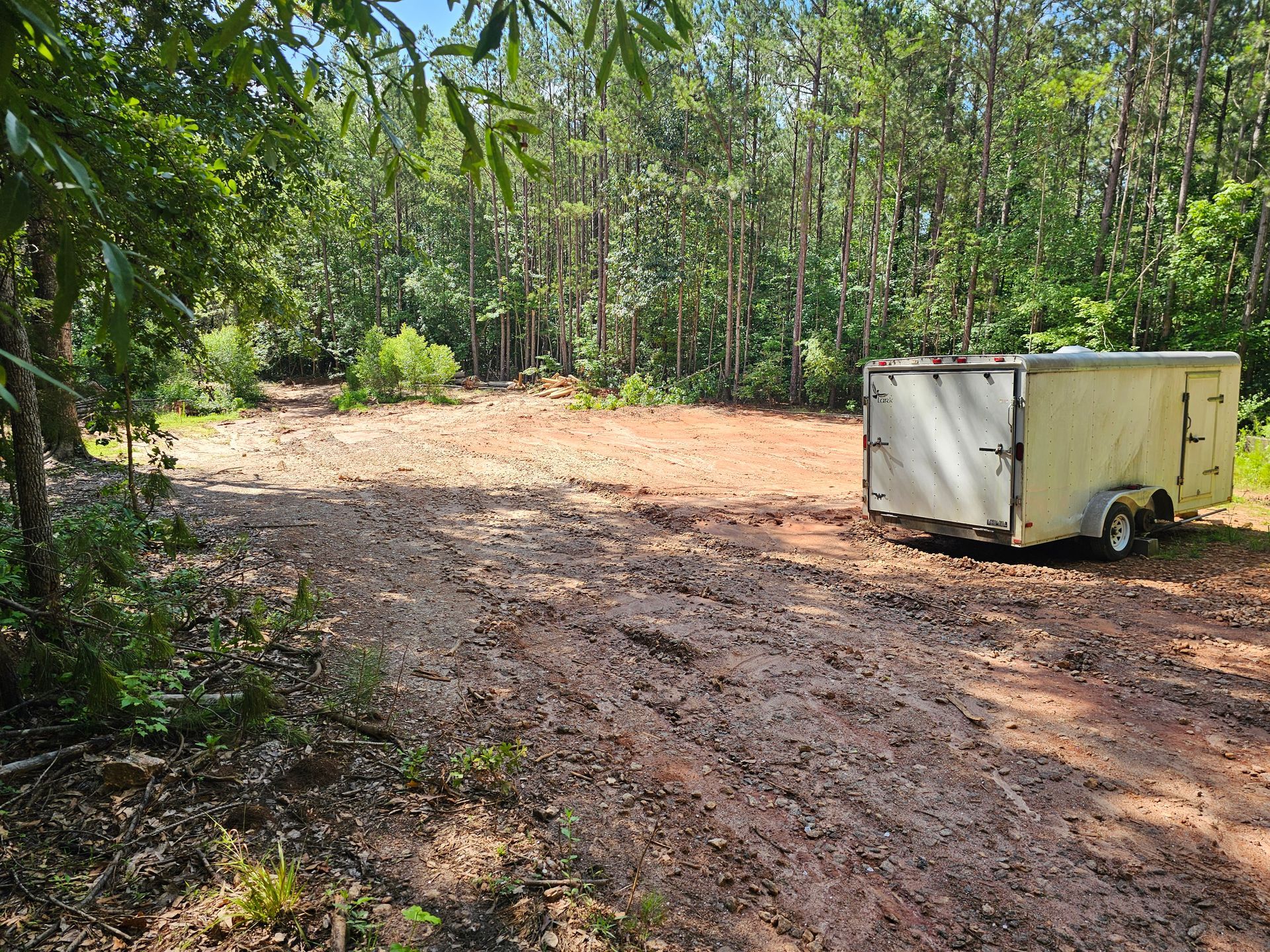 Dirt clearing with a trailer, surrounded by trees.