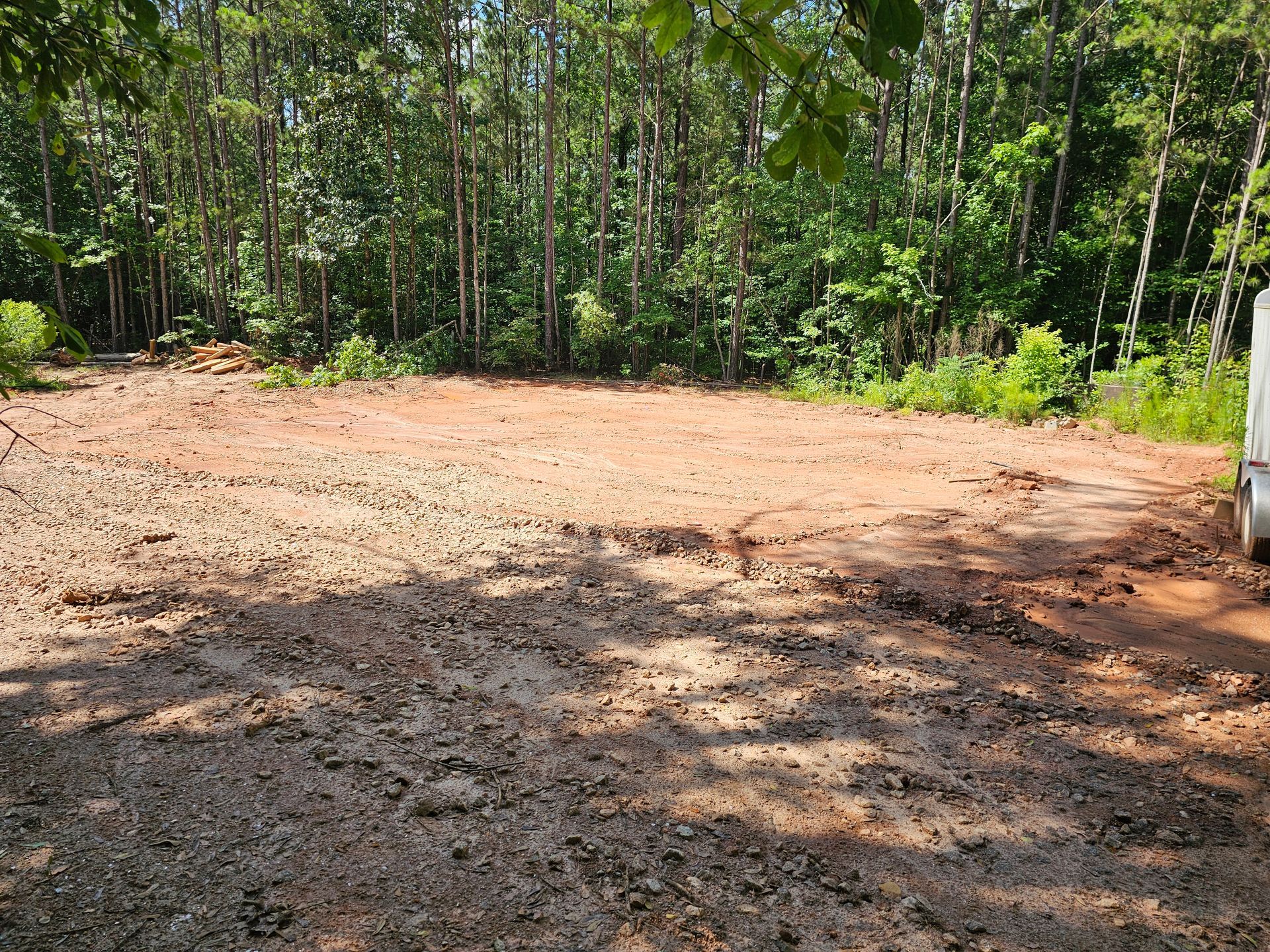 Cleared area of red soil in front of dense forest.