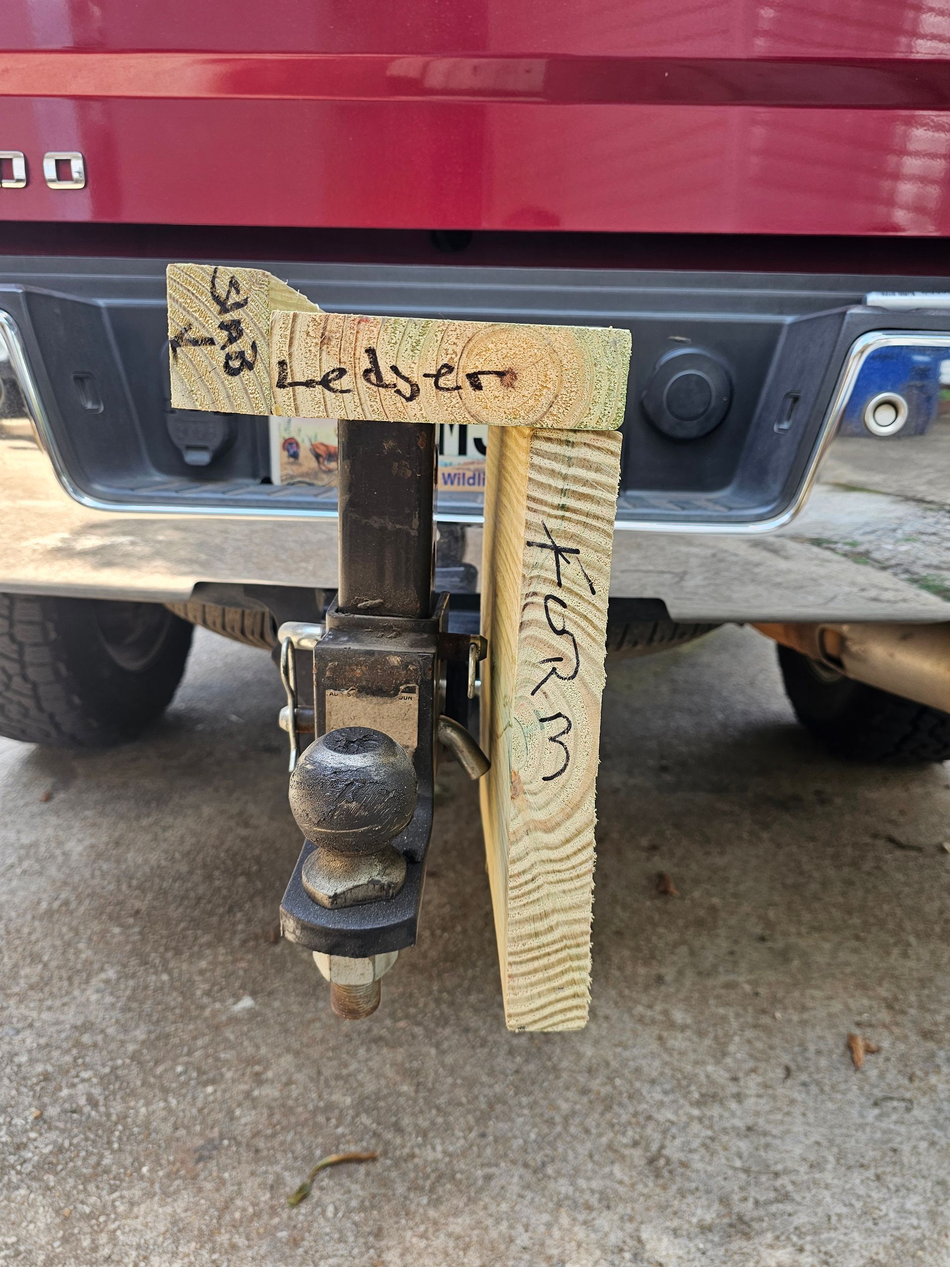 A wooden structure with handwritten text is attached to a truck's trailer hitch.