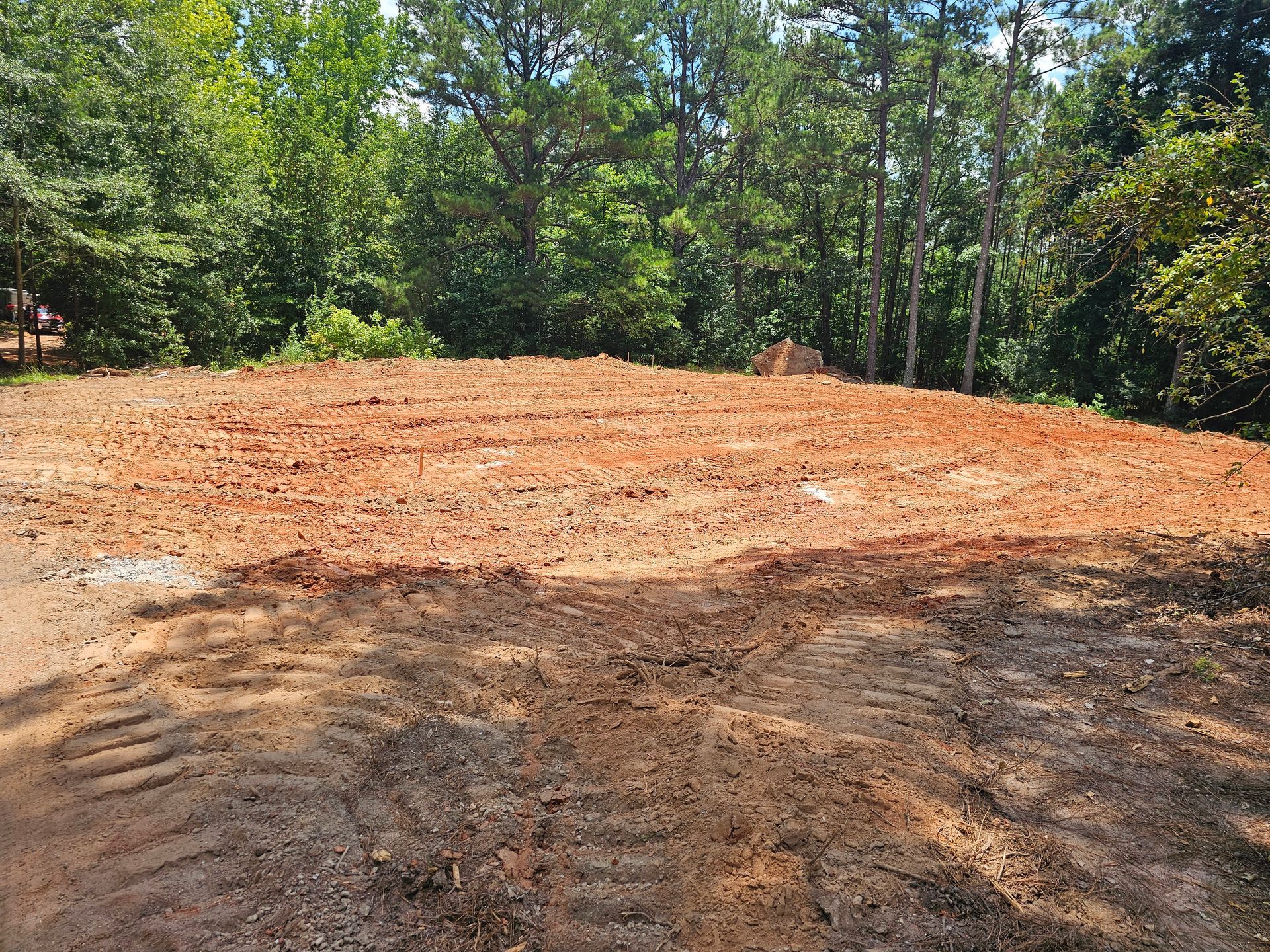 Cleared red clay lot, ready for construction, with trees in the background.