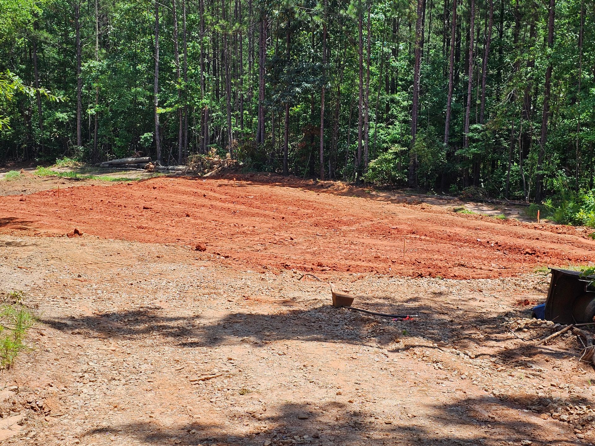 A cleared, red-soil patch in front of a forest; the area is prepared, ready for planting.