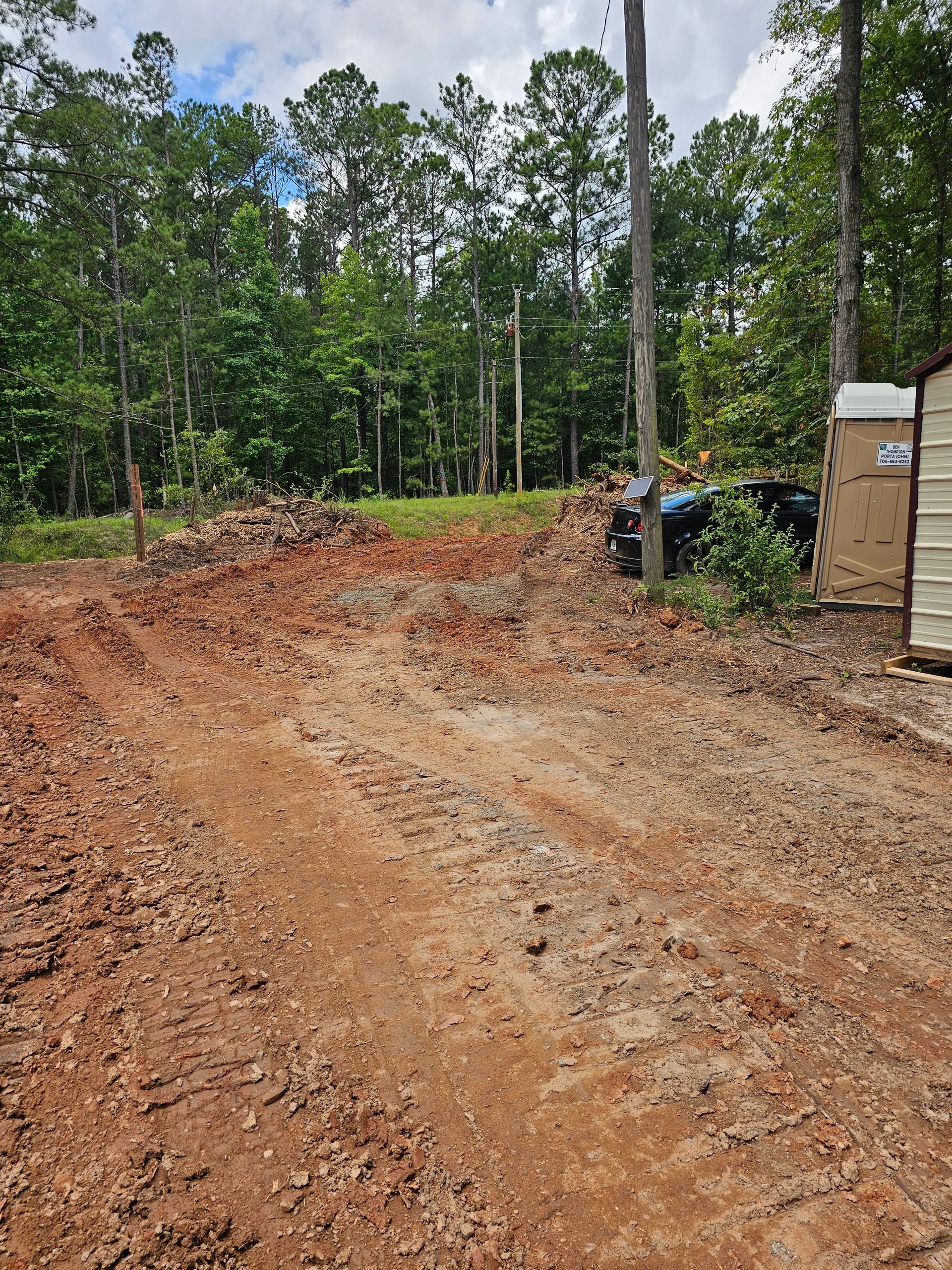 Dirt road leading into a treed area.  A shed is on the right, utility poles in the middle distance.