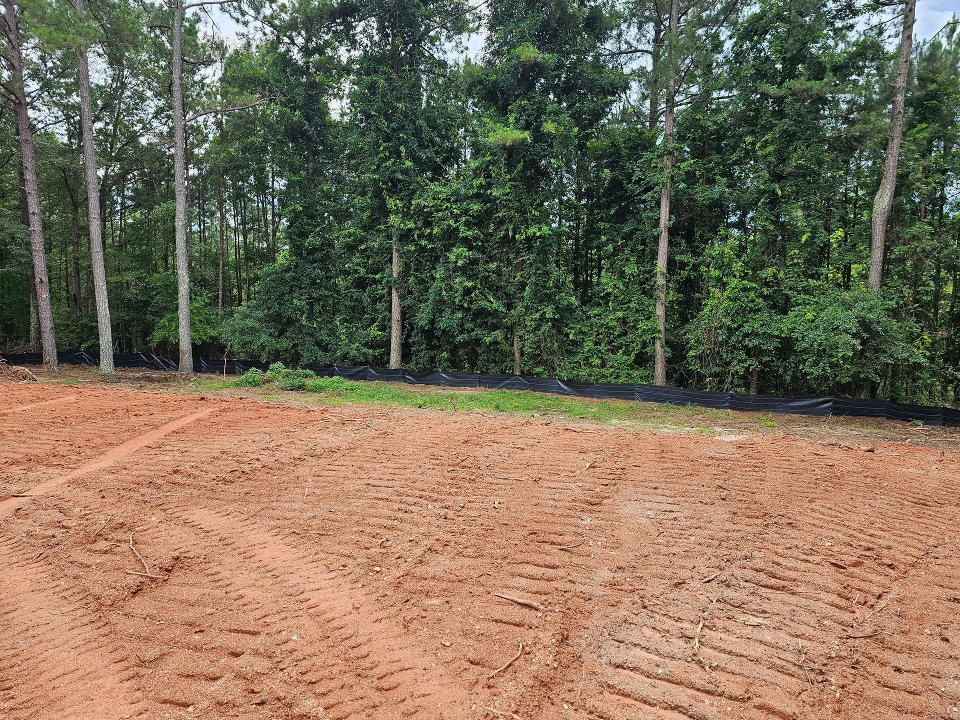Cleared dirt lot with tire tracks, trees in the background, black weed barrier.