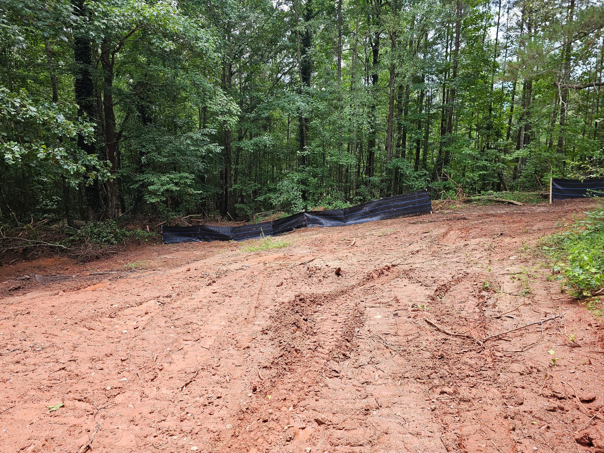 Muddy dirt road with black silt fence leading into a forest.
