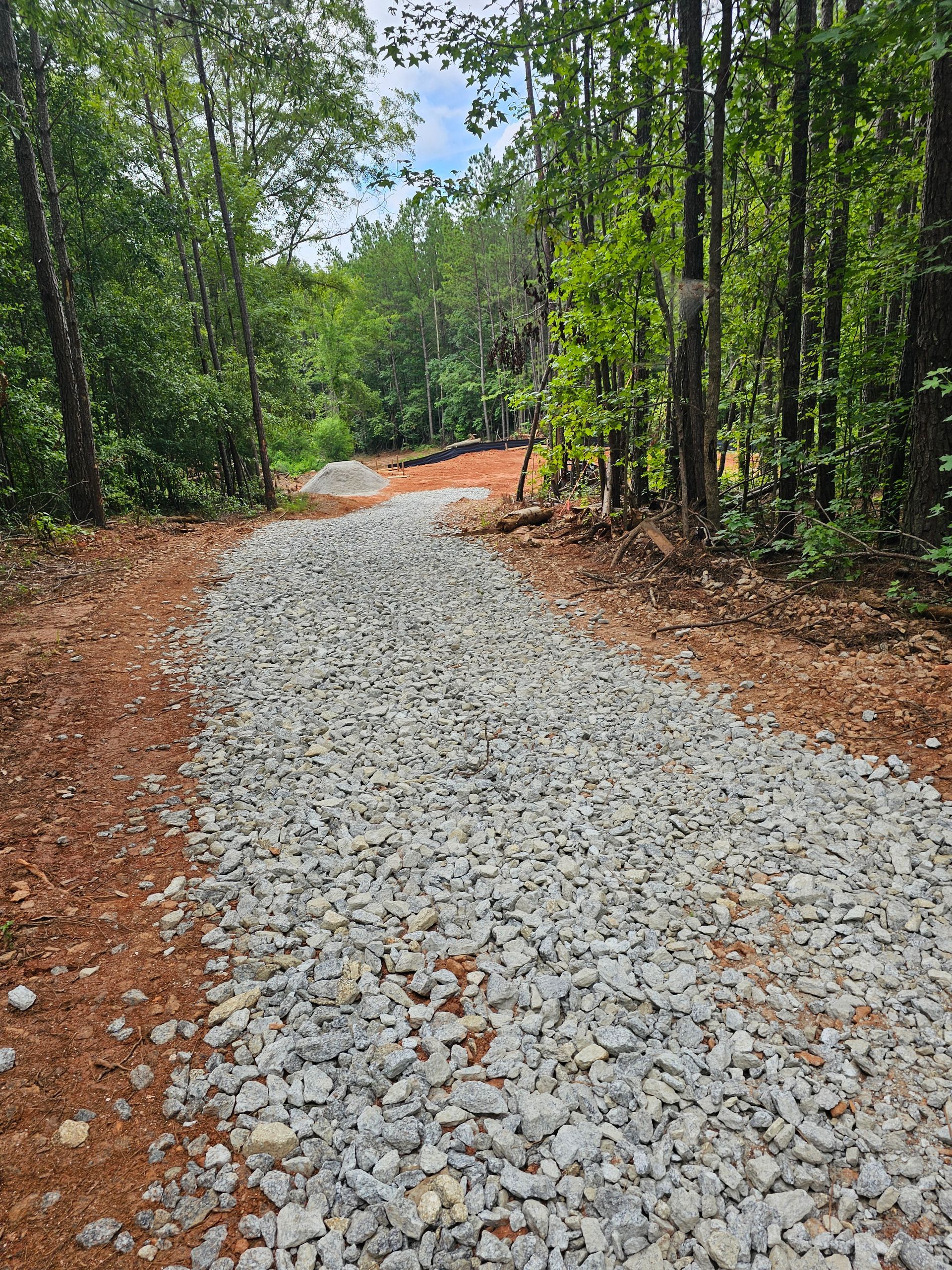 Gravel path through a forest, flanked by trees and red soil, leading uphill.