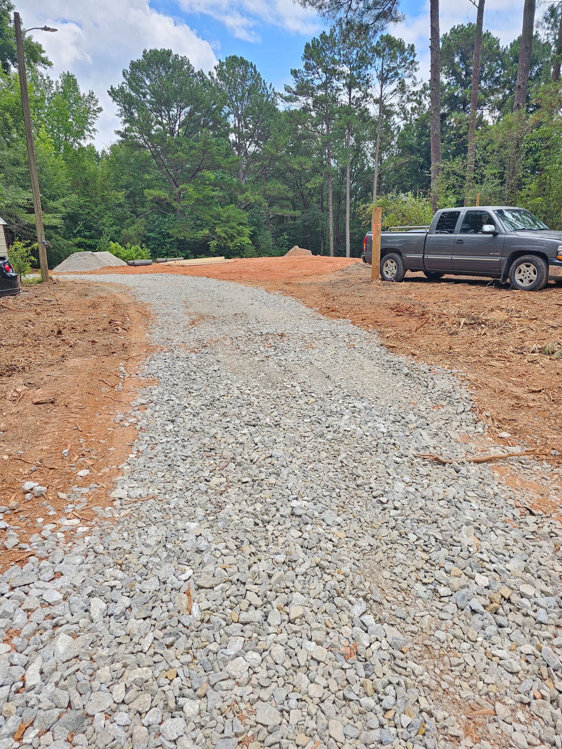 Gravel driveway leading to a cleared, dirt area; a pickup truck is parked nearby.