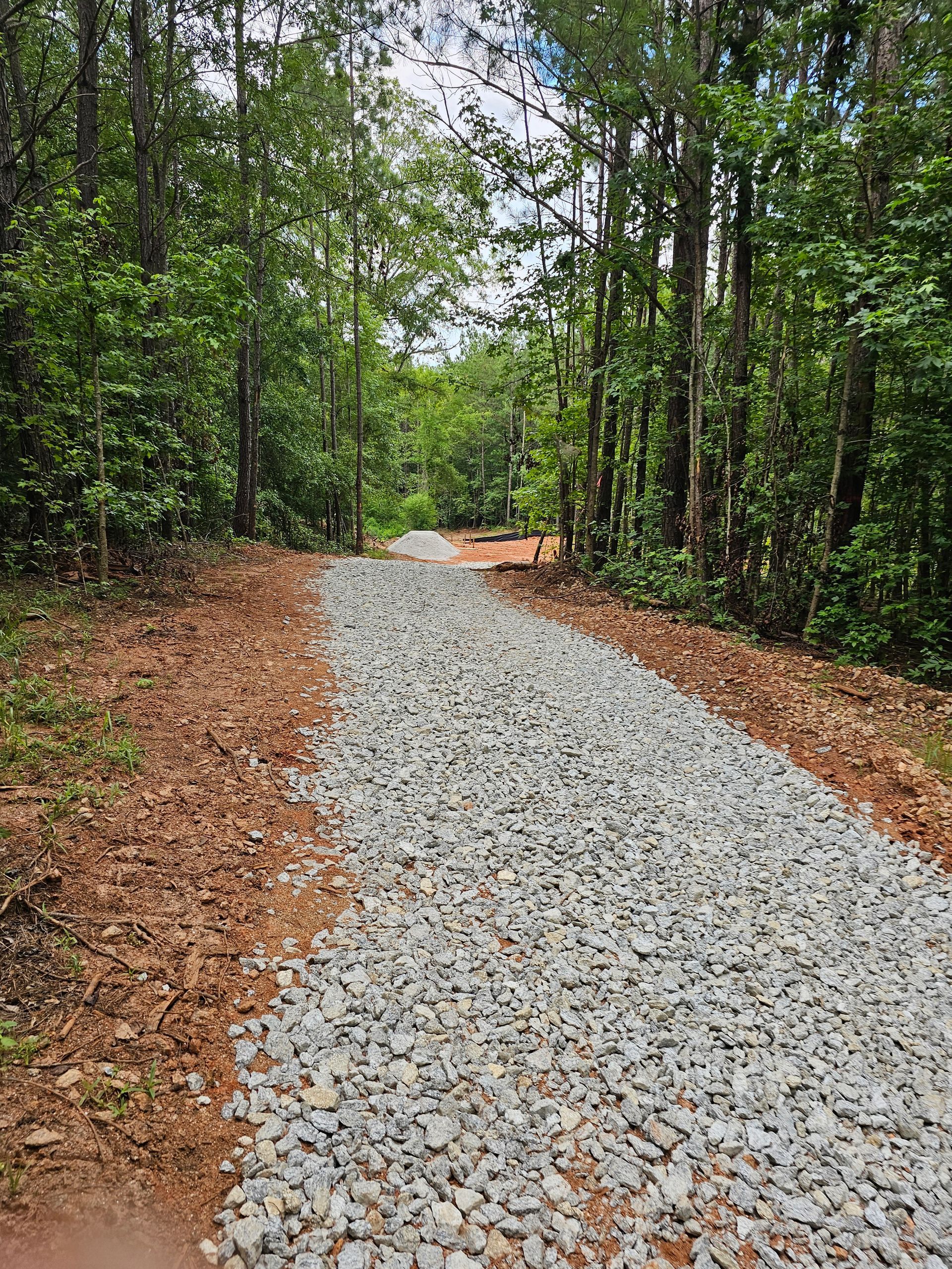 Gravel path through a forest. Trees line the sides. Blue sky visible at the end of the path.