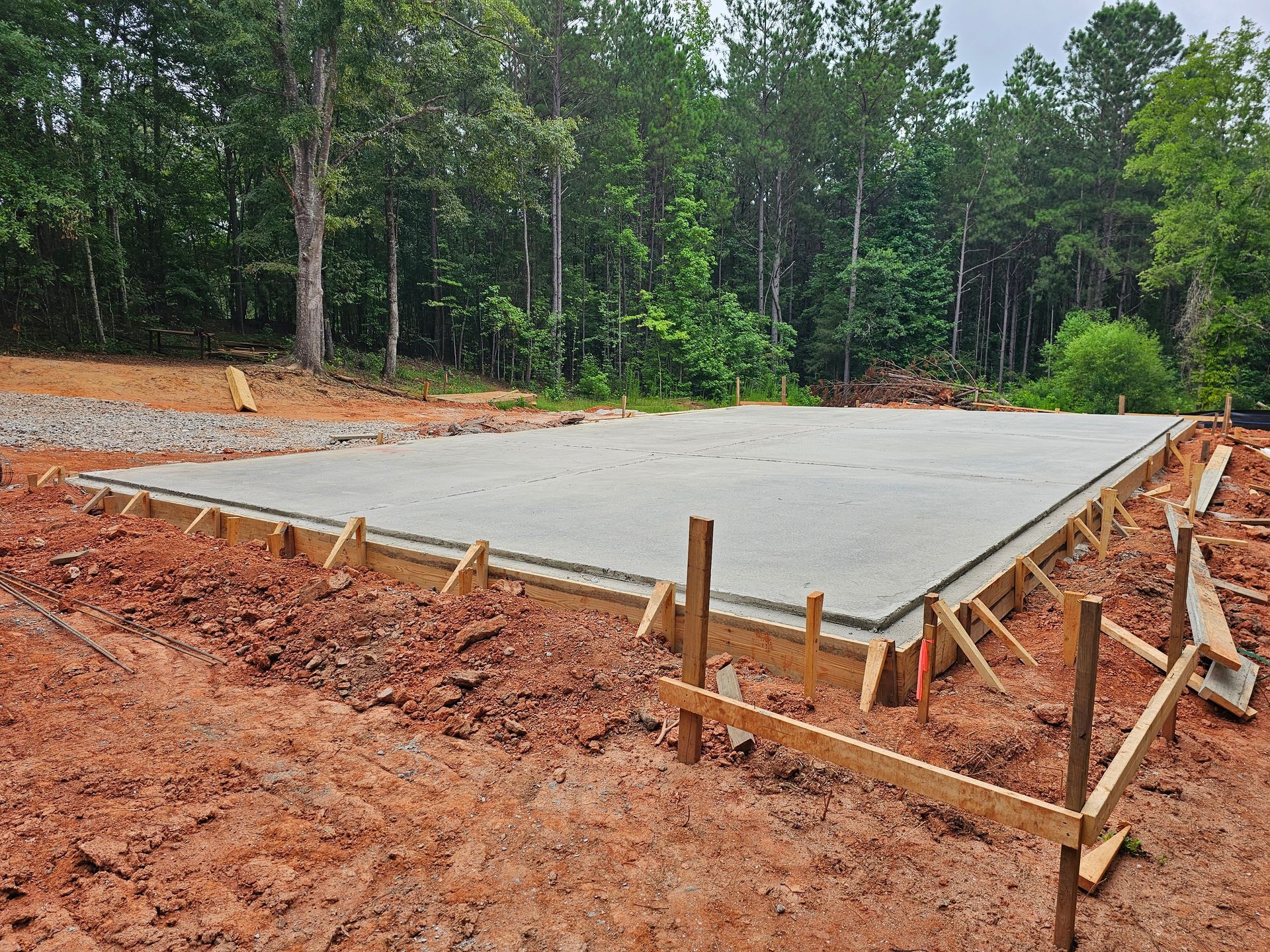Concrete foundation with wooden frame, set in dirt, trees in background.