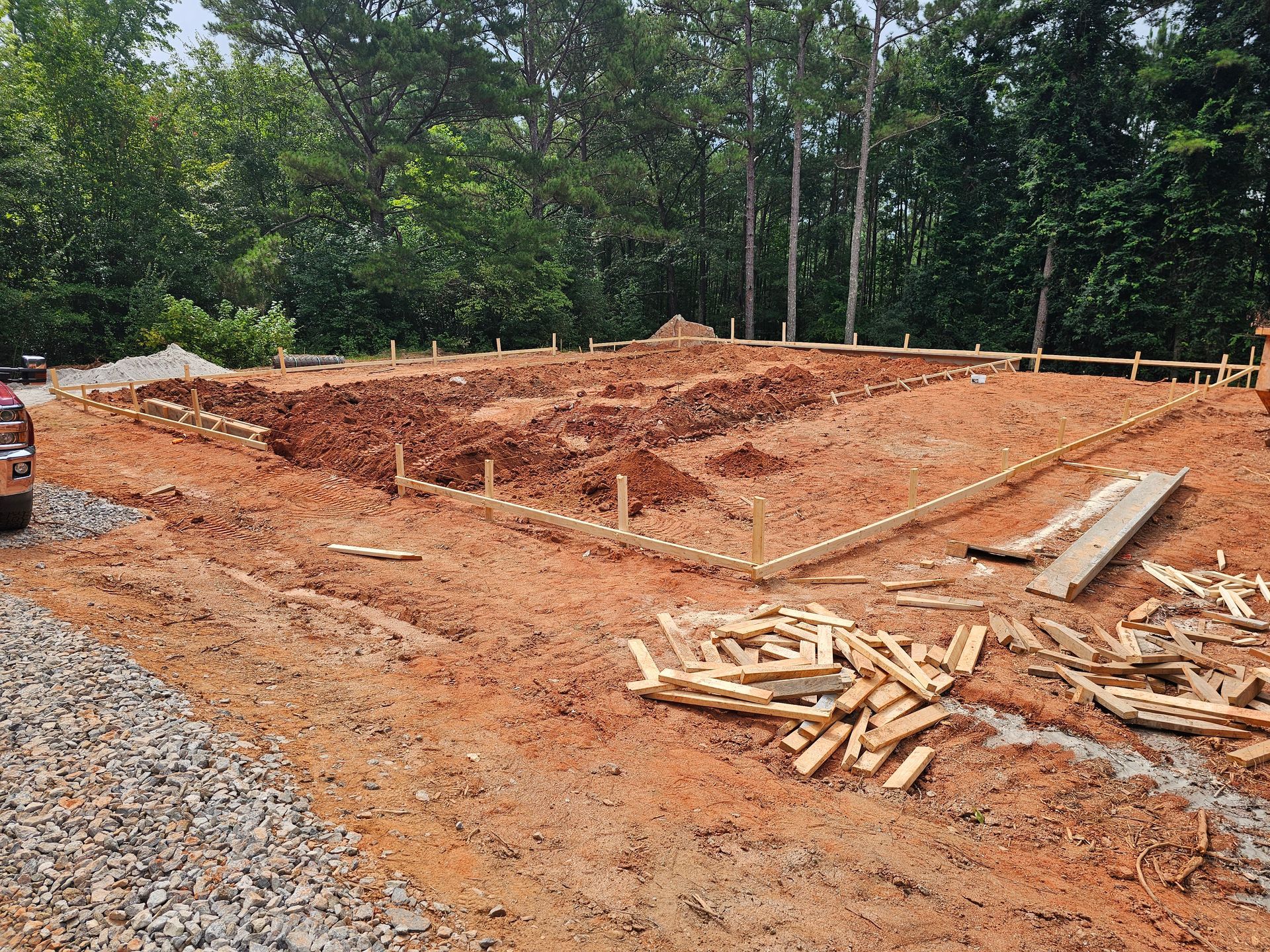 Construction site with exposed red dirt, wooden framing, and building foundation being laid.