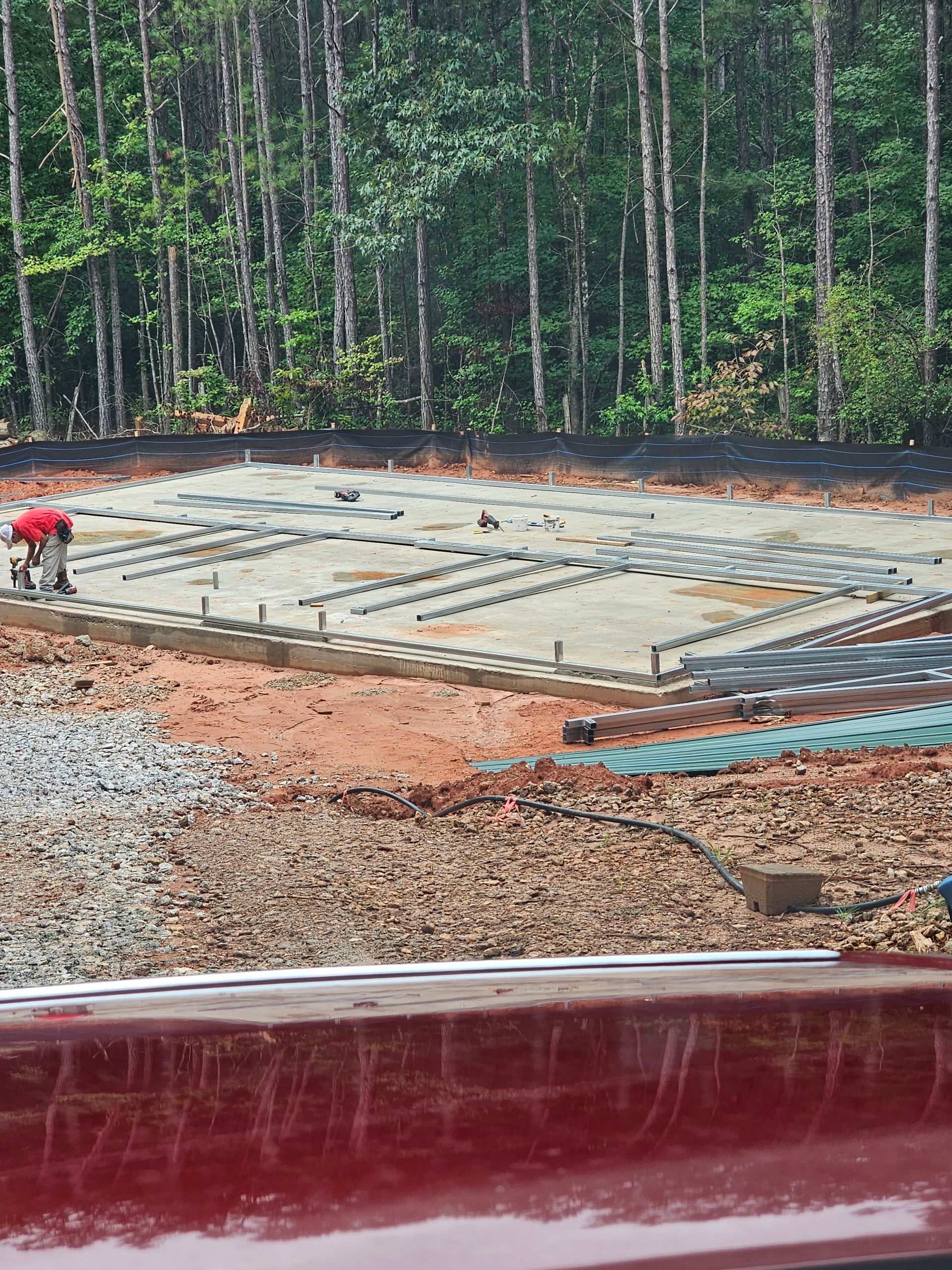 Construction site with a partially built foundation. Workers in red shirts. Forest background.