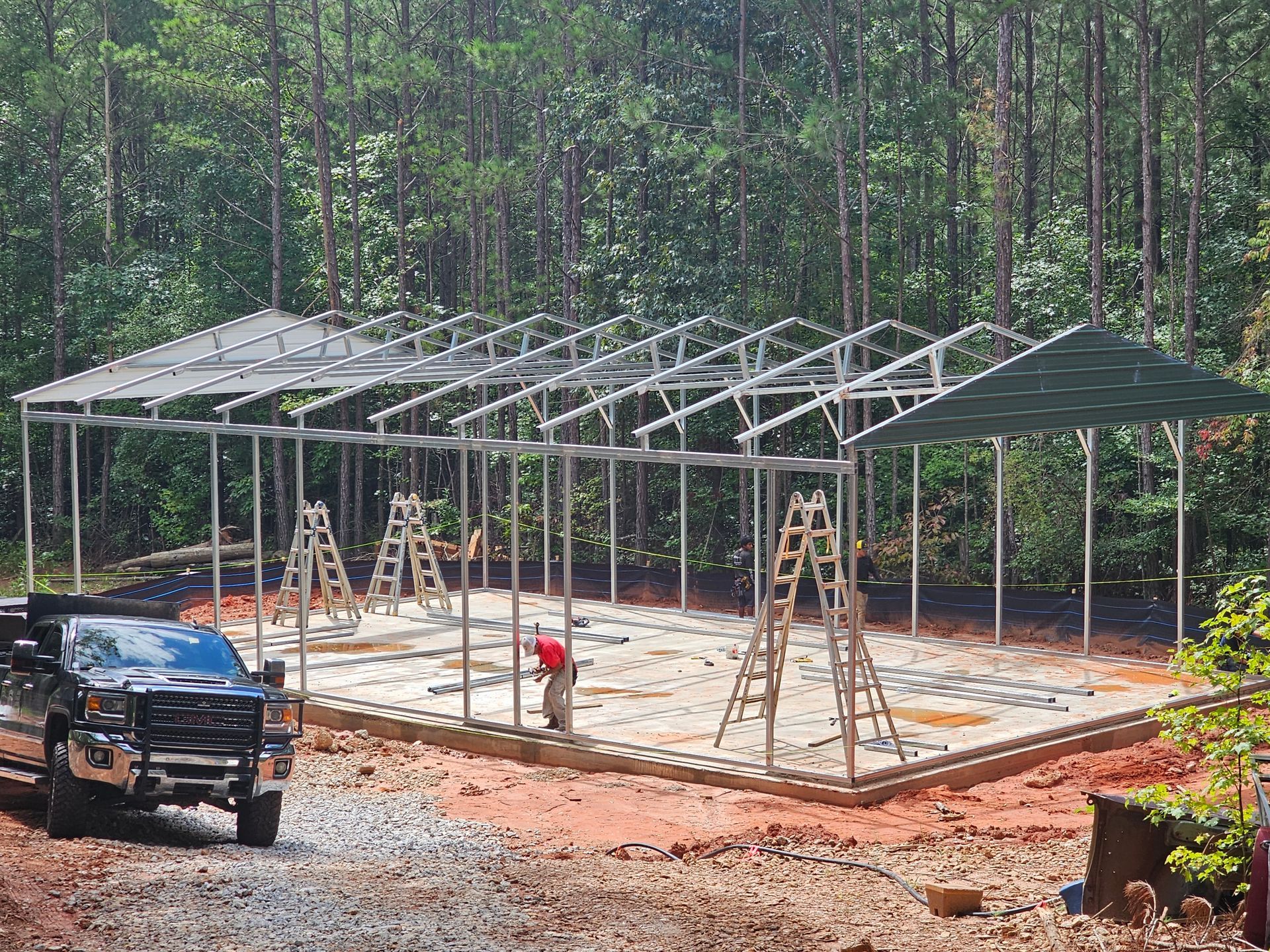 Metal structure under construction; workers, truck, ladders. Forest background.