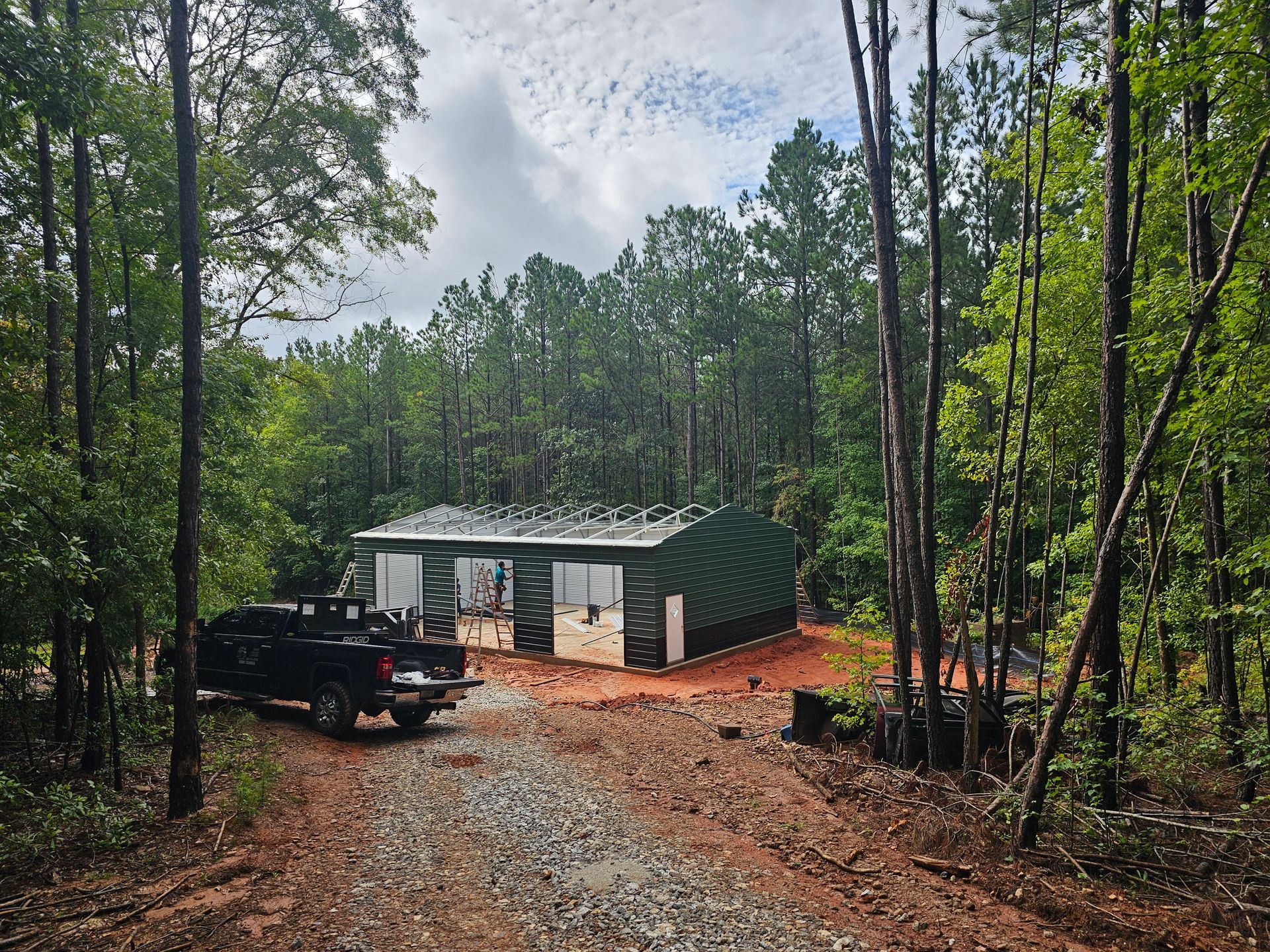 A dark green metal building in a wooded area with a truck parked in front.