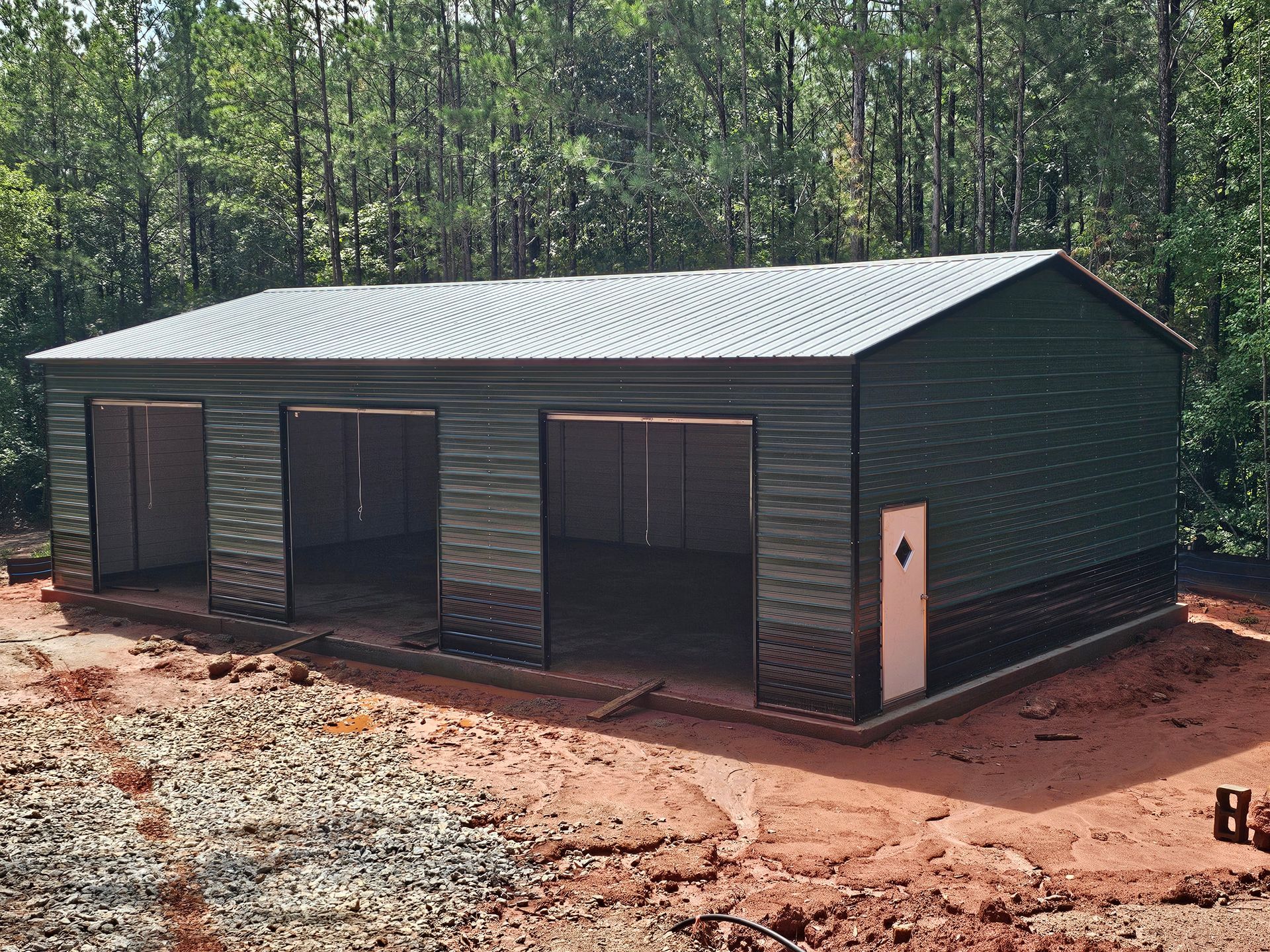 Green metal garage with three bays and a side door, set against a backdrop of trees.