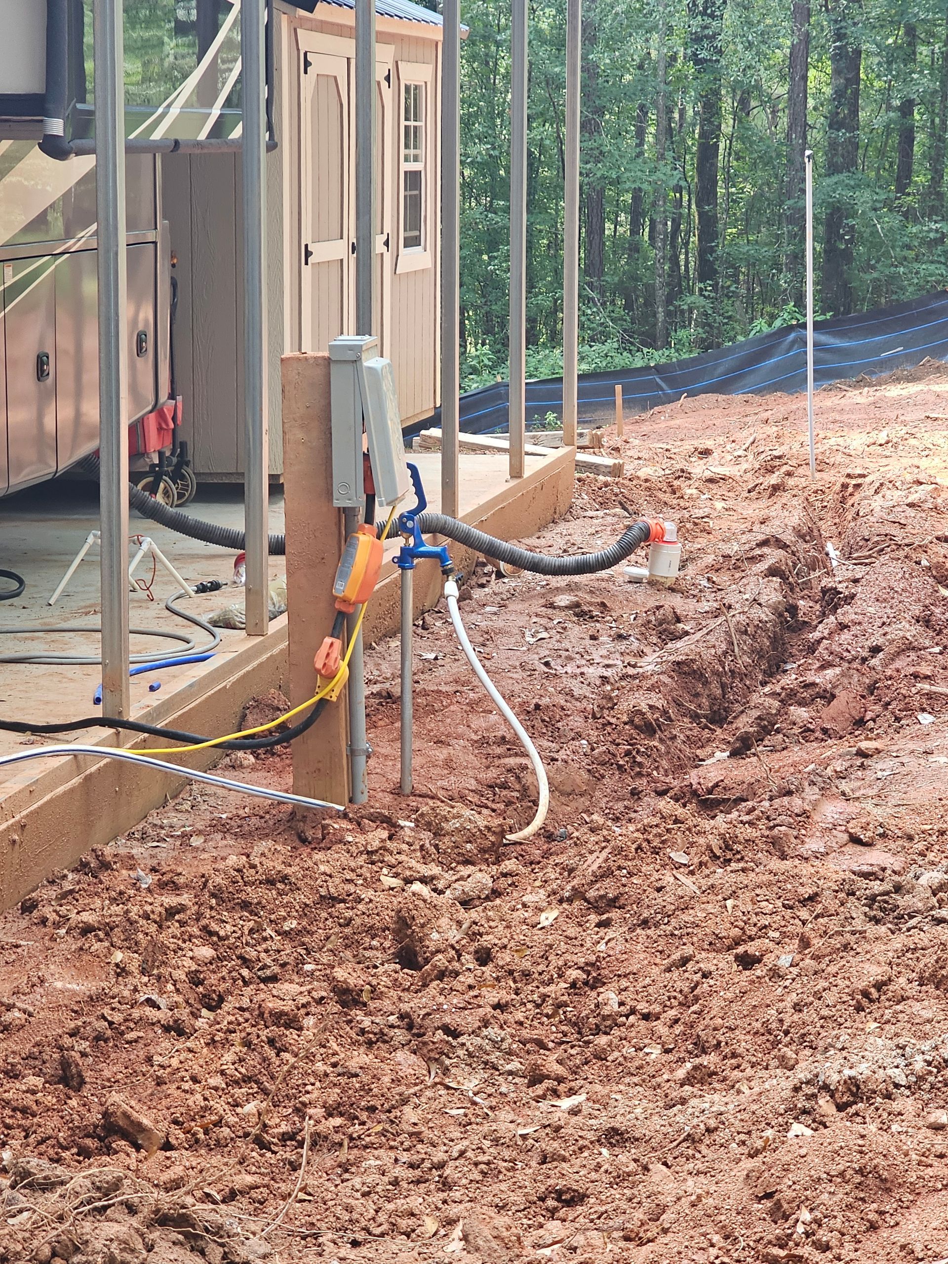 Construction site with electrical conduit and wiring near a building; red dirt and a trench are visible.