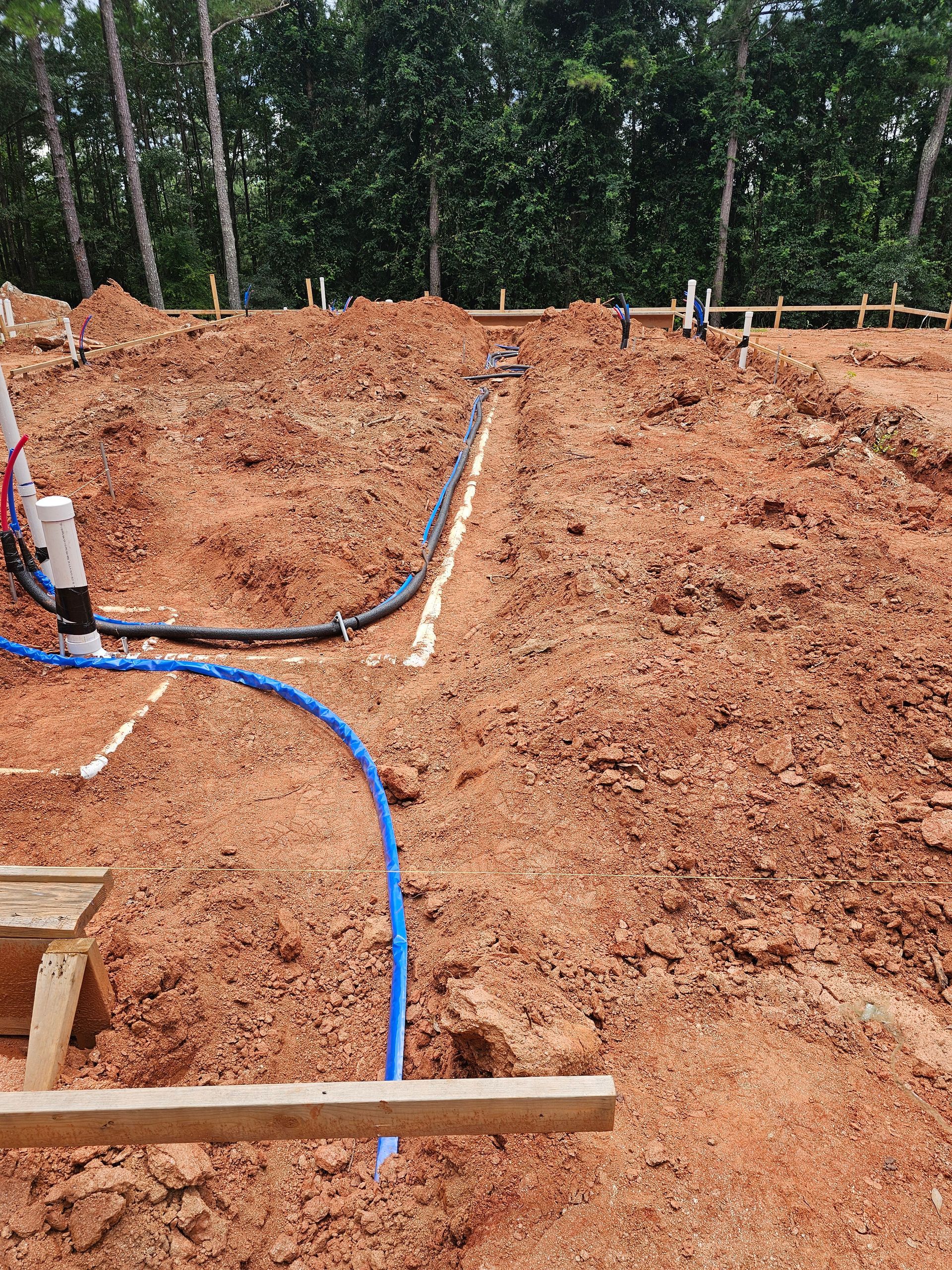 Dirt excavation site with blue and black pipes, and white PVC in the ground.