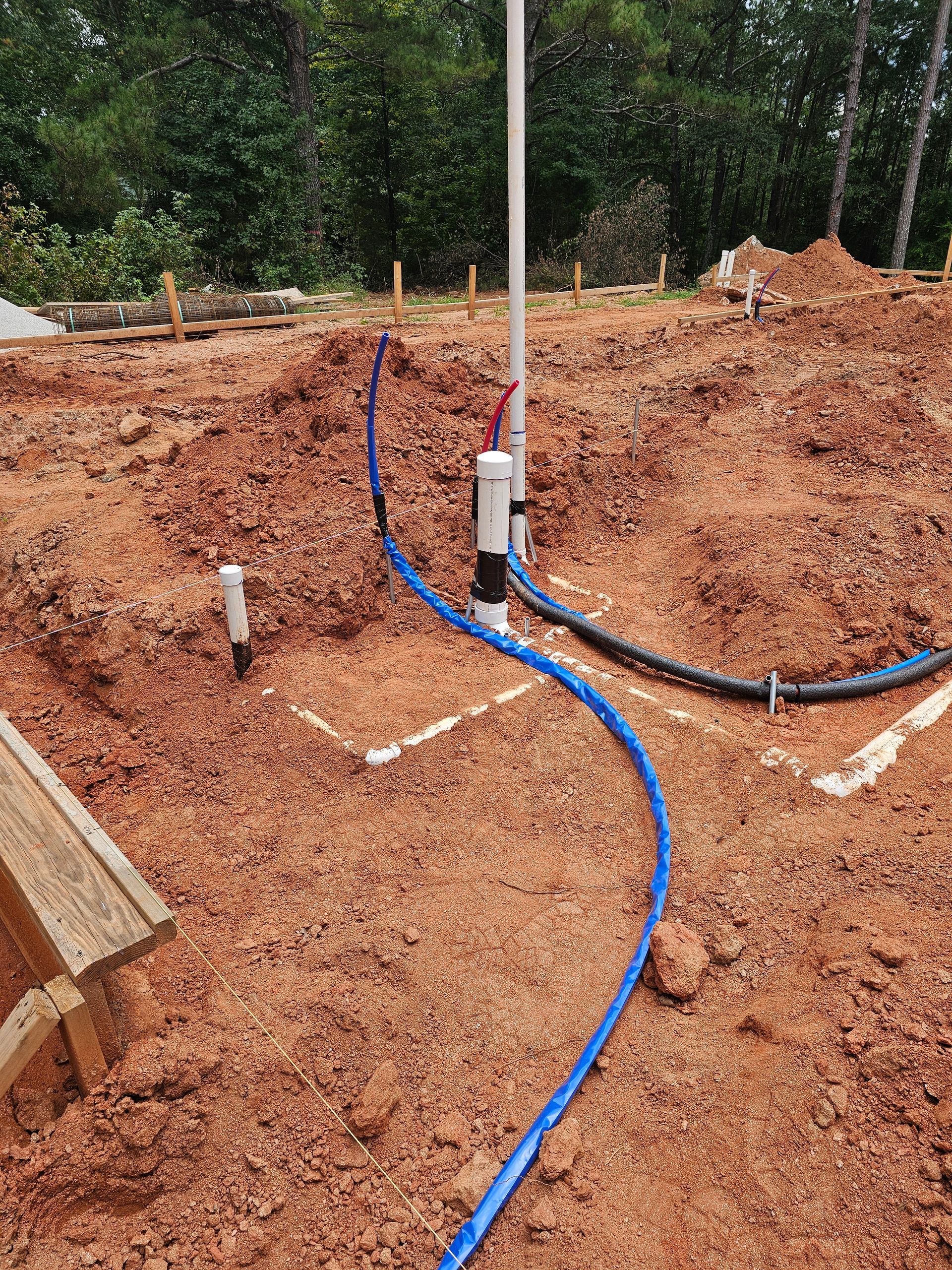 Construction site with buried blue water pipes and plumbing fixtures in red soil.