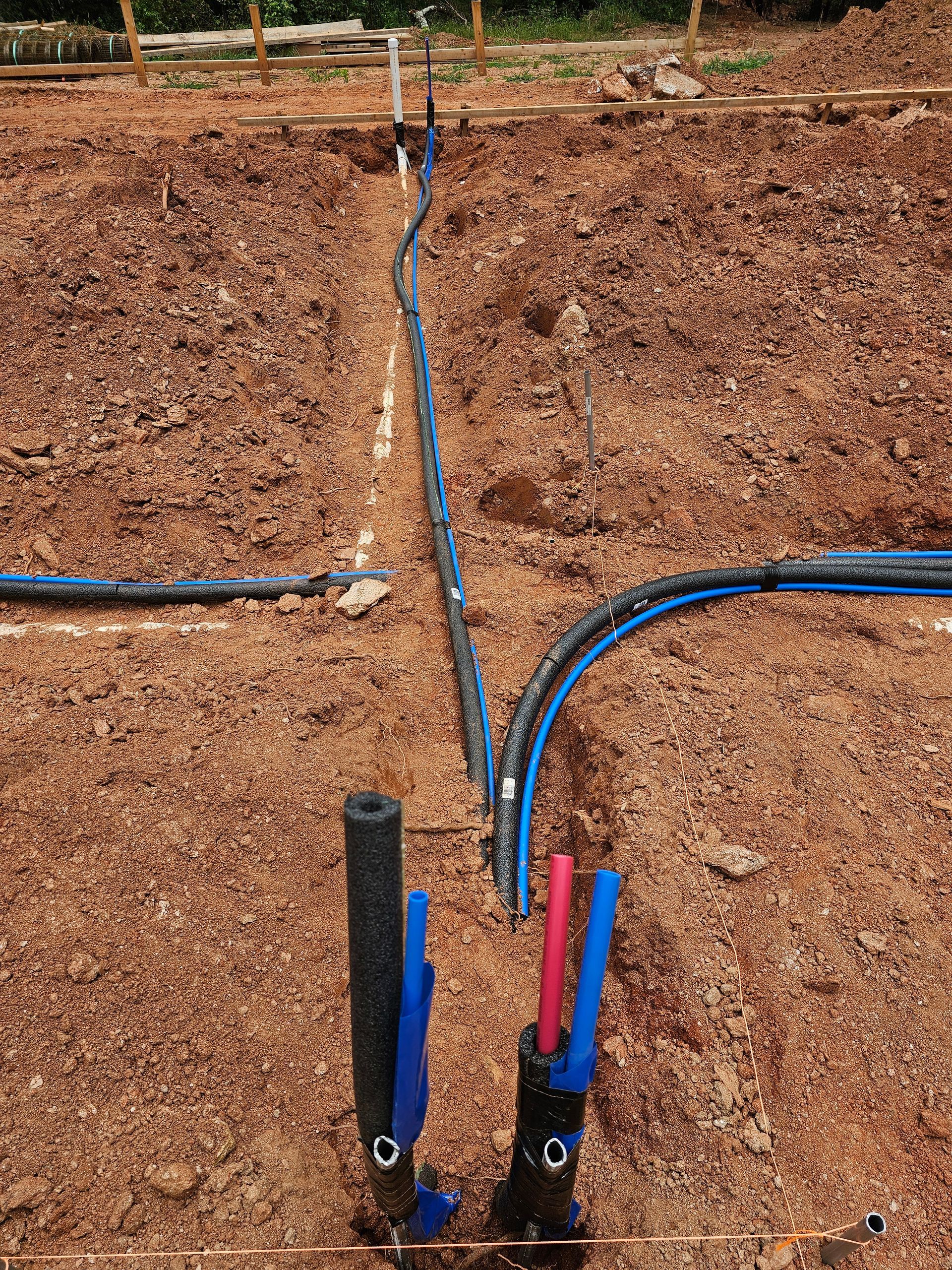 Trenched ground with blue and black pipes, and red and blue plastic pipes emerging.