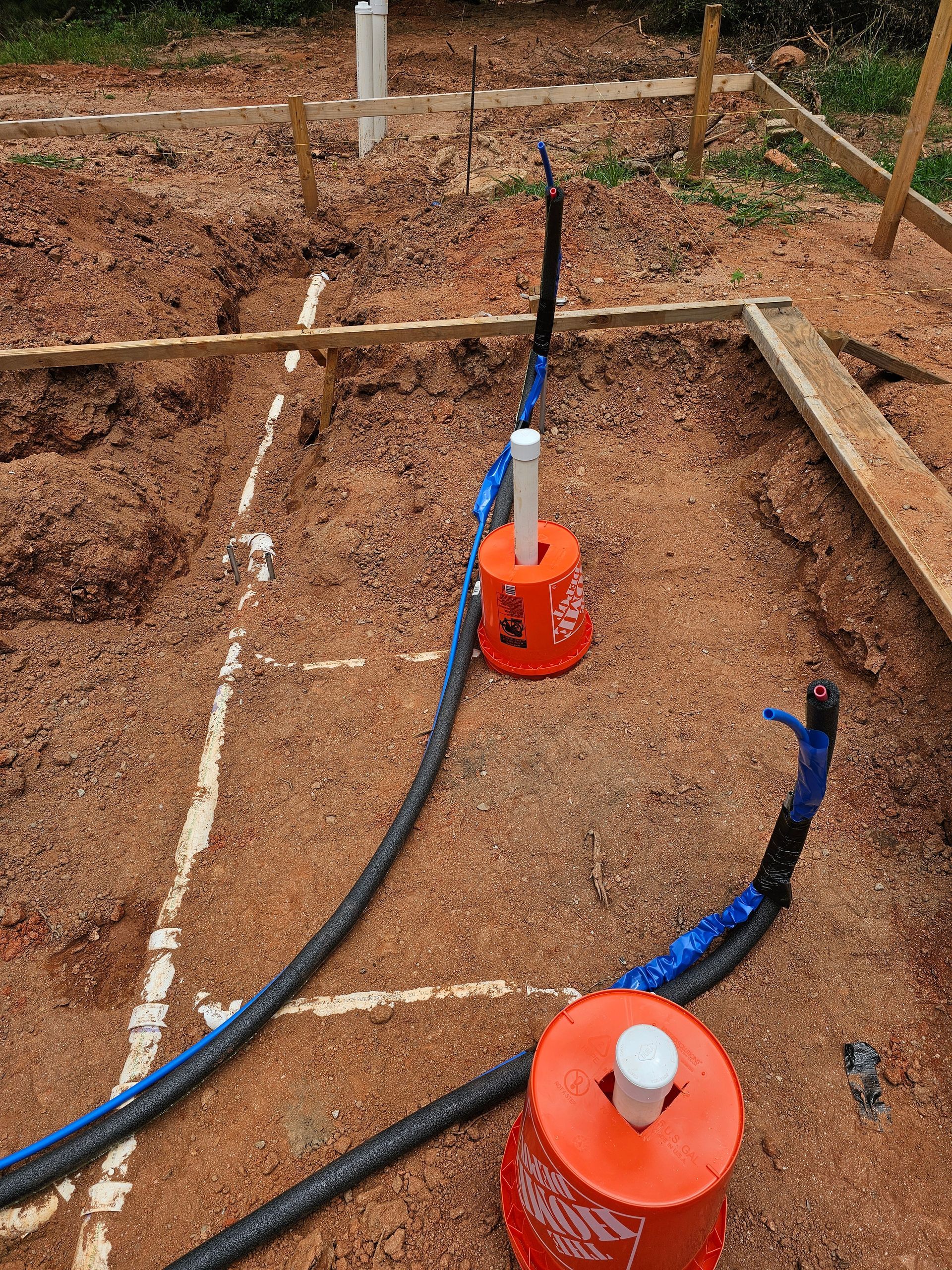 Construction site with orange buckets and pipes in a dirt foundation.