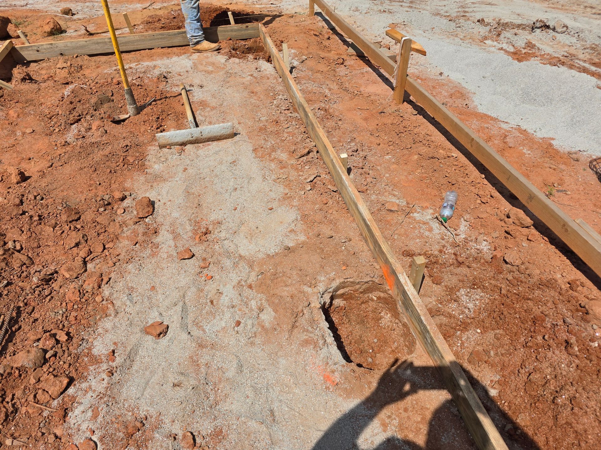 Construction site with wooden forms for concrete. Red dirt and gravel visible.