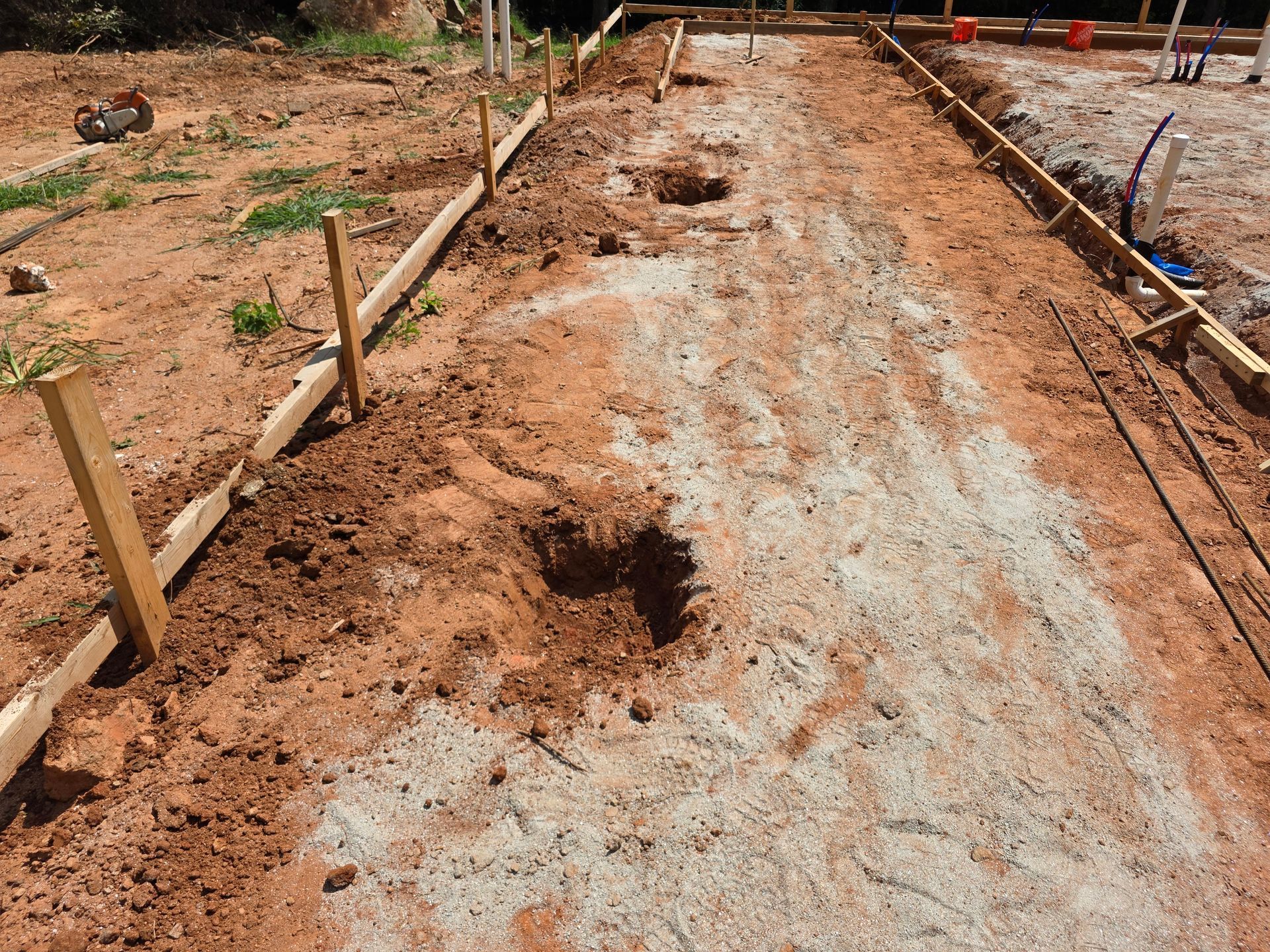 Construction site with wooden forms and excavated holes in dirt, prepared for concrete.