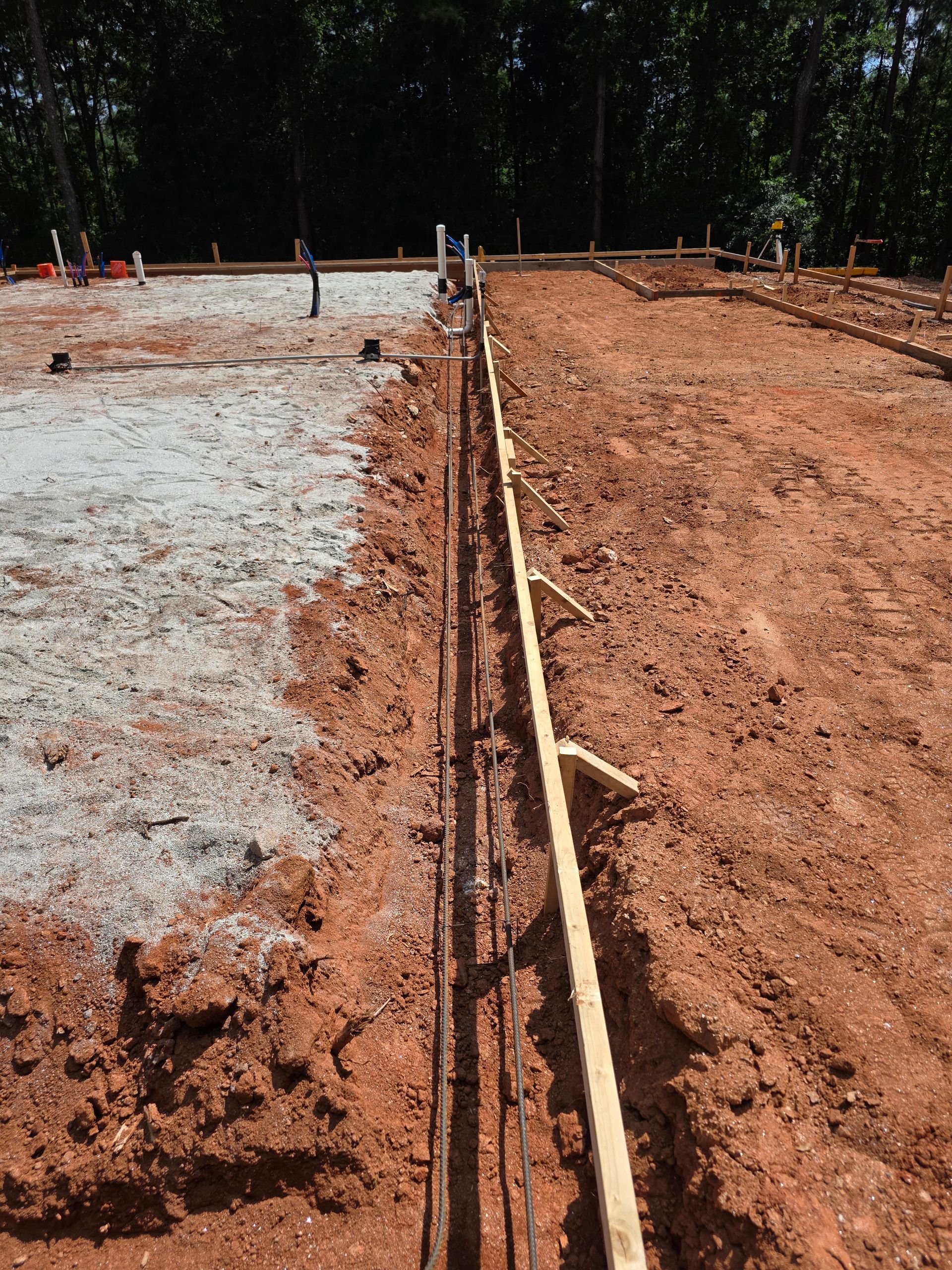 Construction site with foundation forms, rebar, and gravel on red soil.
