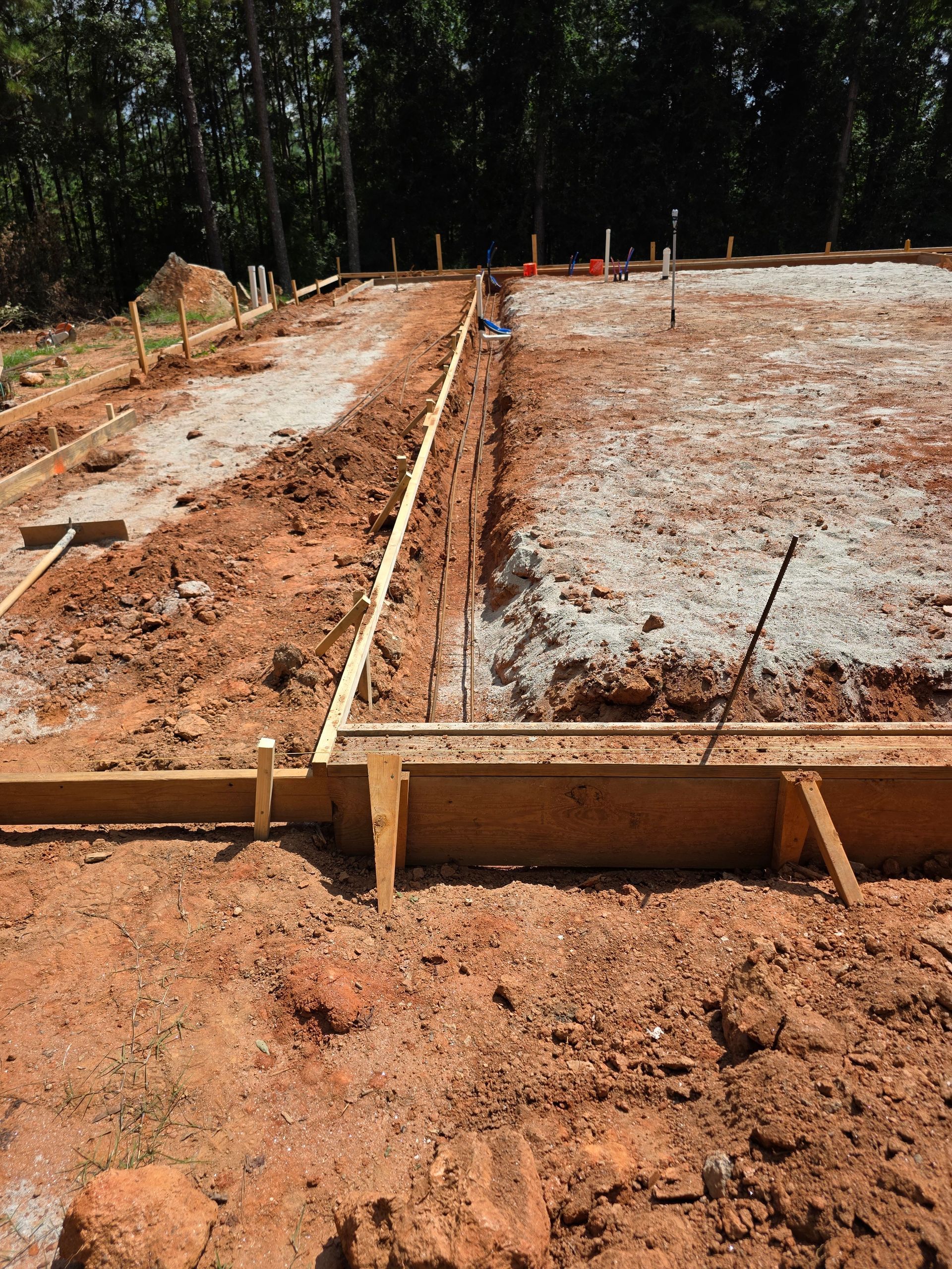 Construction site with wooden forms and excavated trenches in red soil.