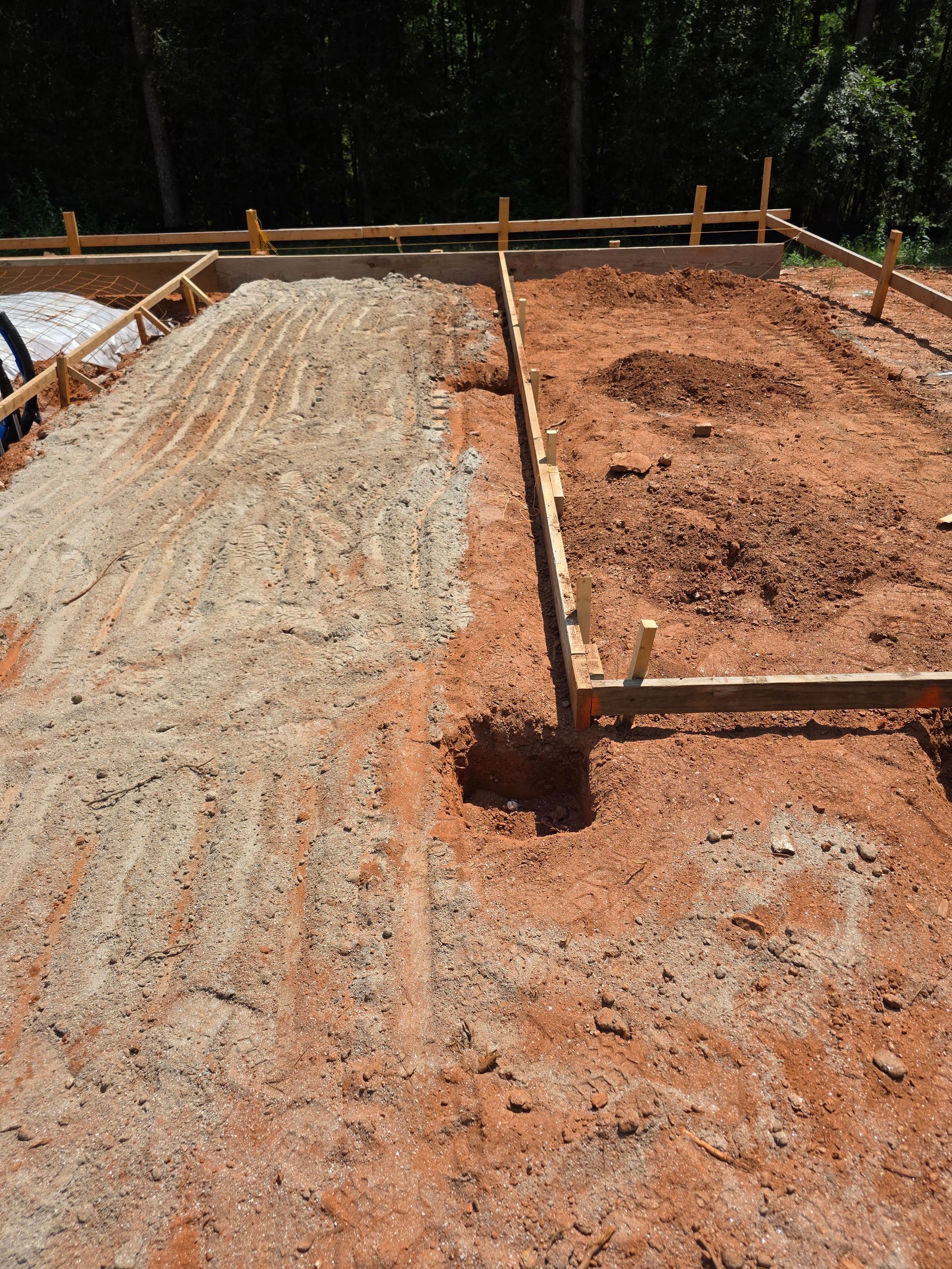 Construction site with wooden frame and reddish dirt, showing two dirt colors and a hole.