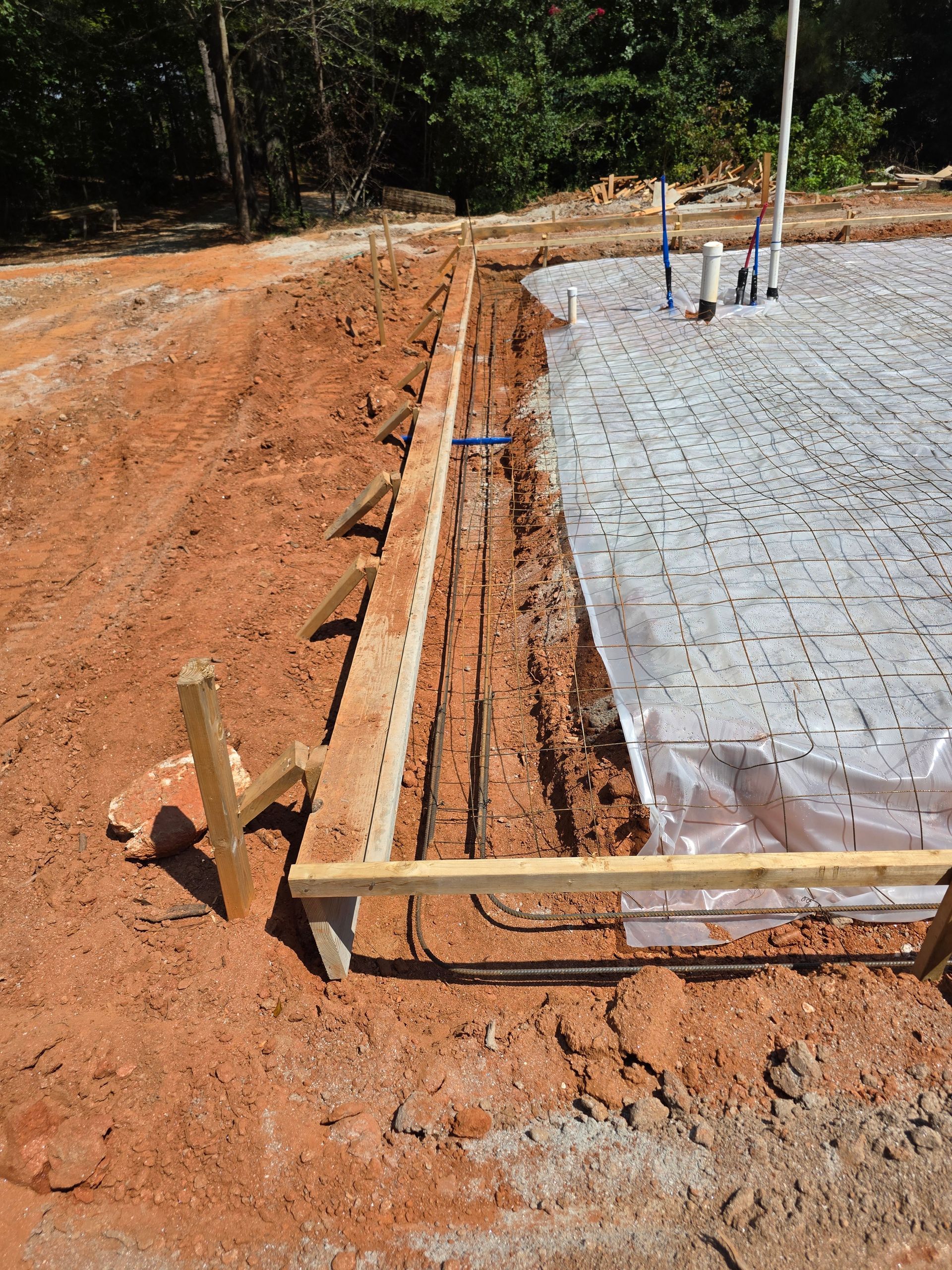 Construction site showing a concrete foundation with plumbing and wooden framing in dirt.