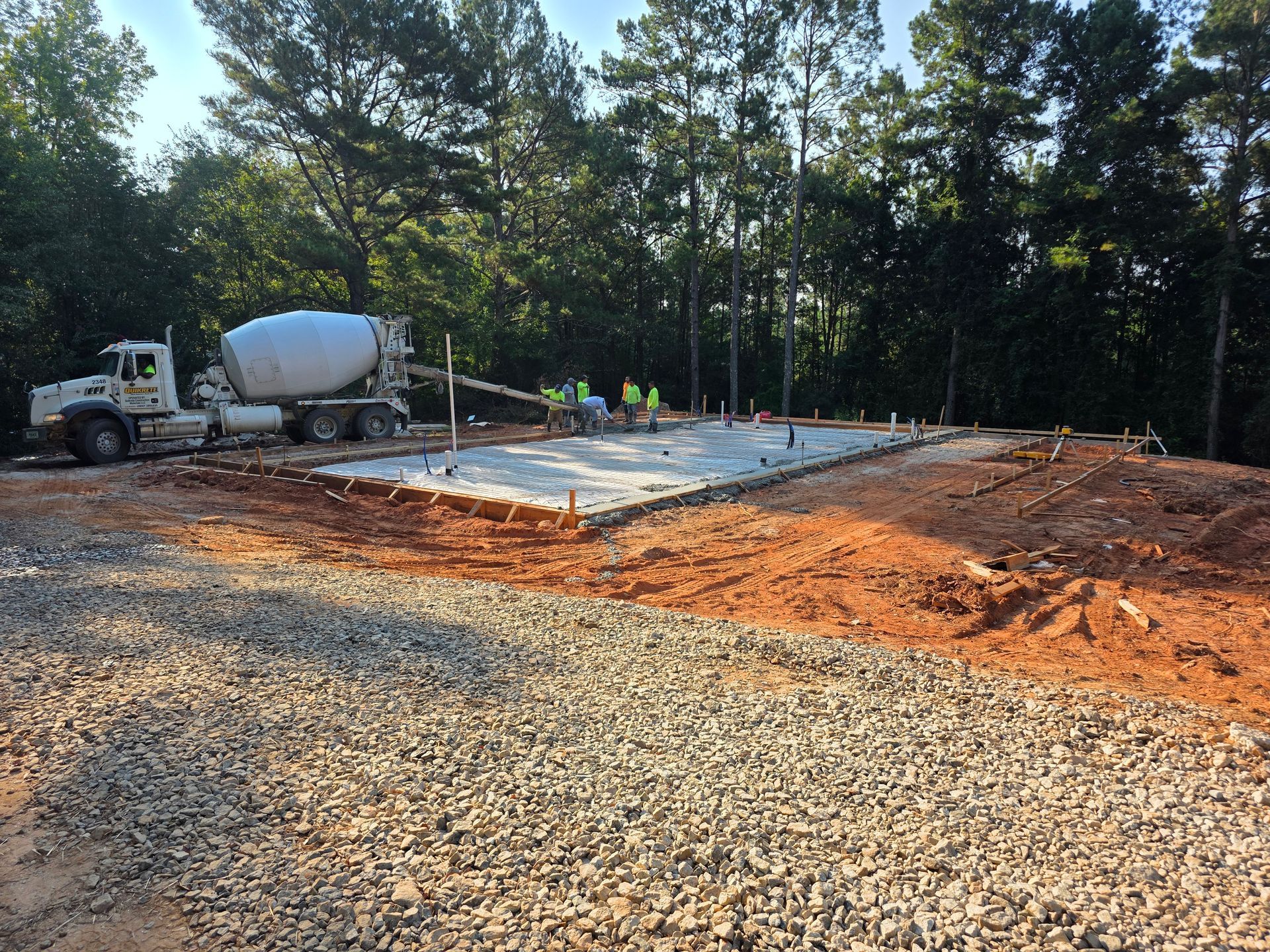 Cement truck pouring concrete onto a prepared foundation at a construction site in a wooded area.