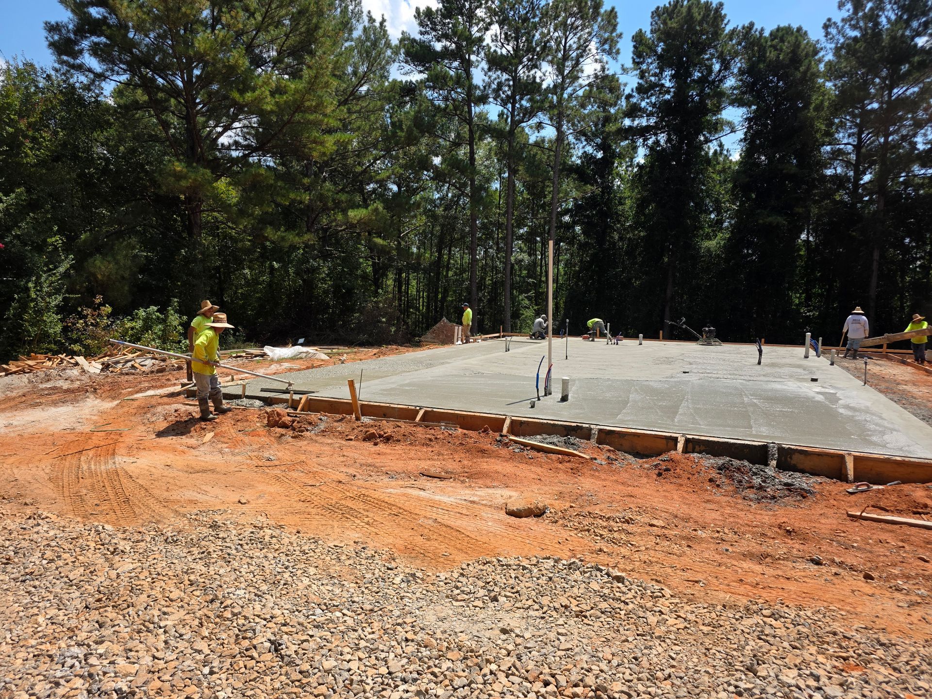 Newly poured concrete foundation with workers in a wooded area.