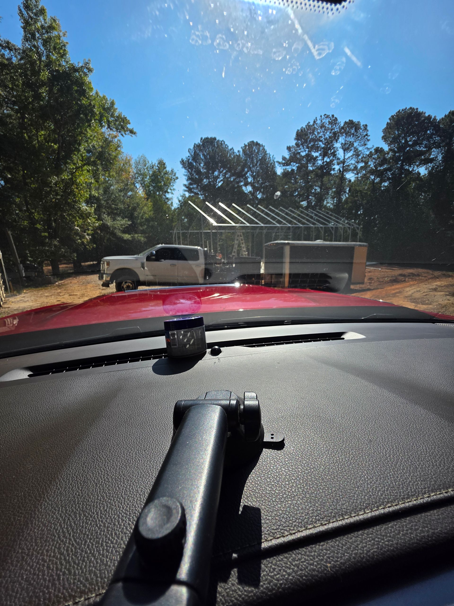 View from inside a red vehicle of a white truck and trailer near a metal structure on a sunny day.