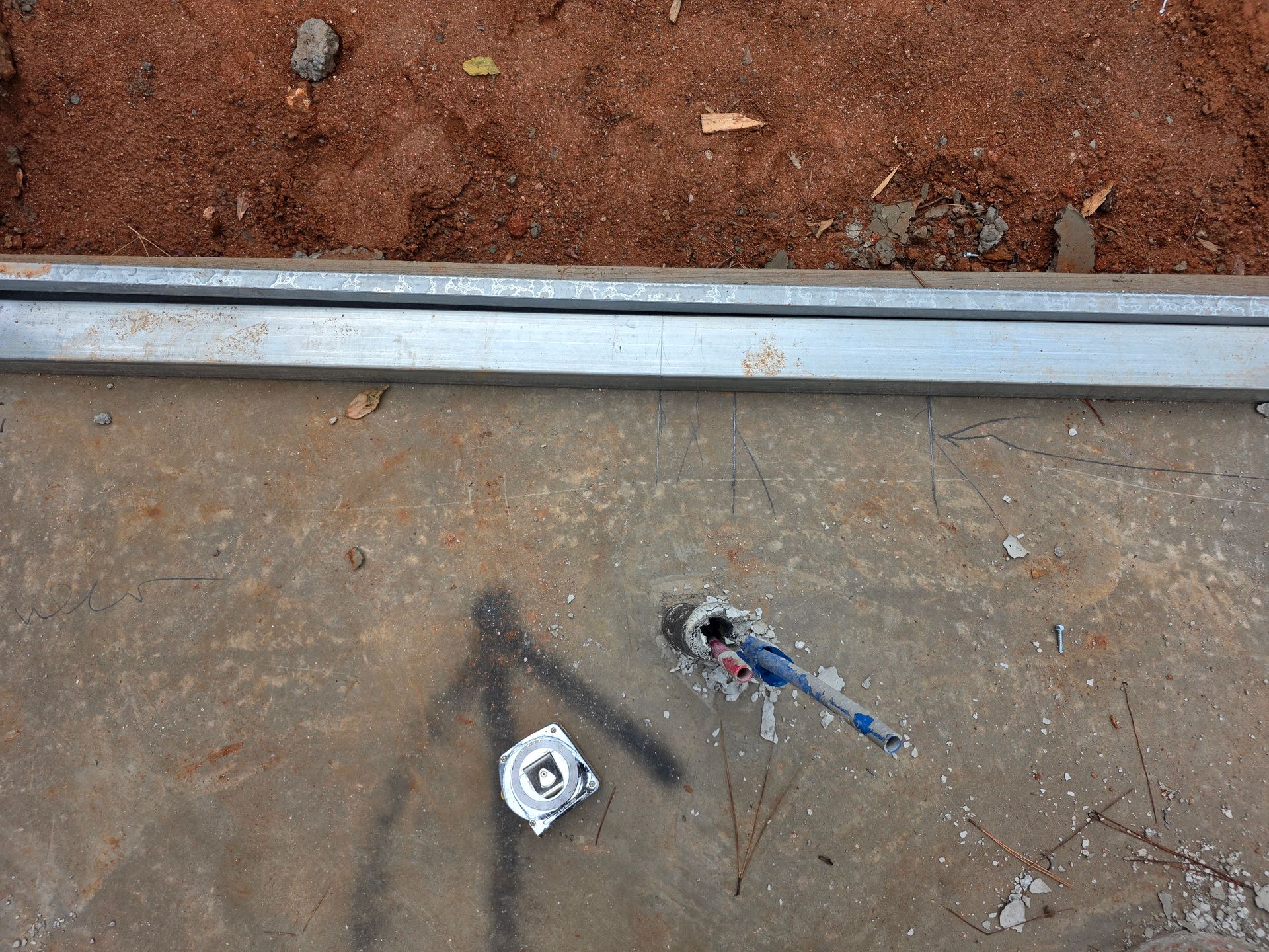 Concrete floor with a metal bar, a tape measure, and a hole with a wire.