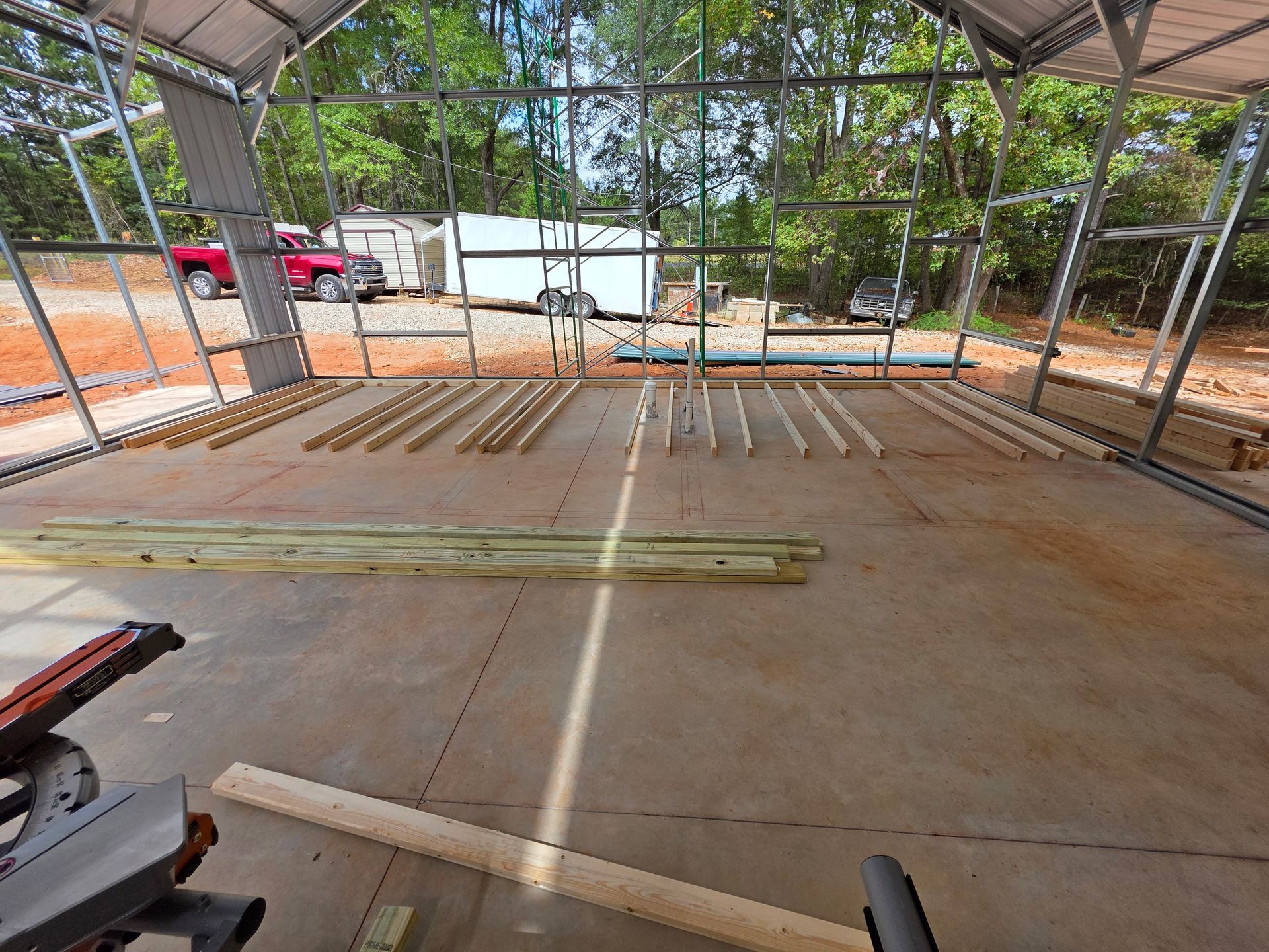 Construction site: metal frame building interior with lumber. A red truck and trailer are visible outside.
