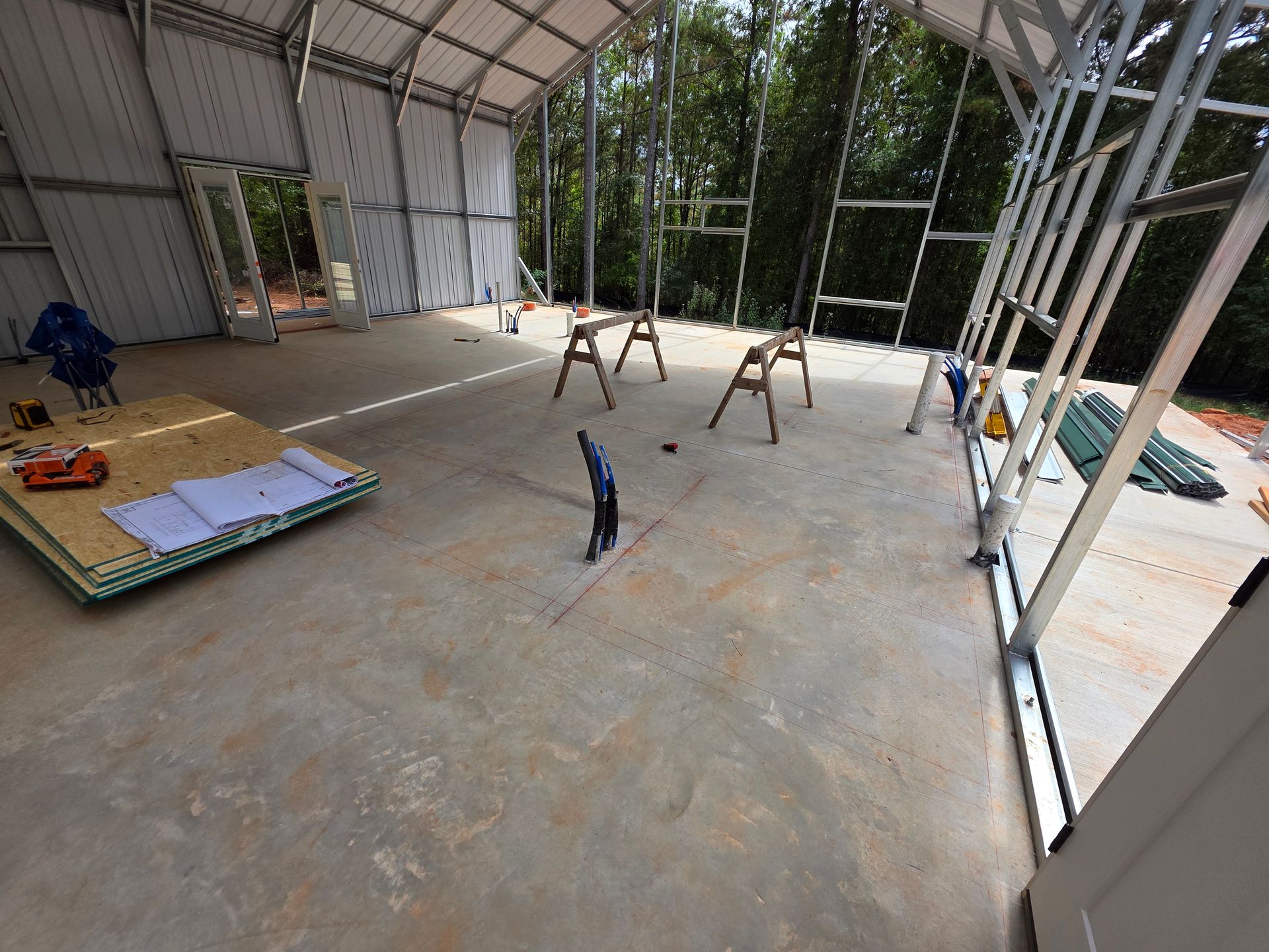 Interior of a metal building under construction, concrete floor, with tools, wood panels, and a person working.