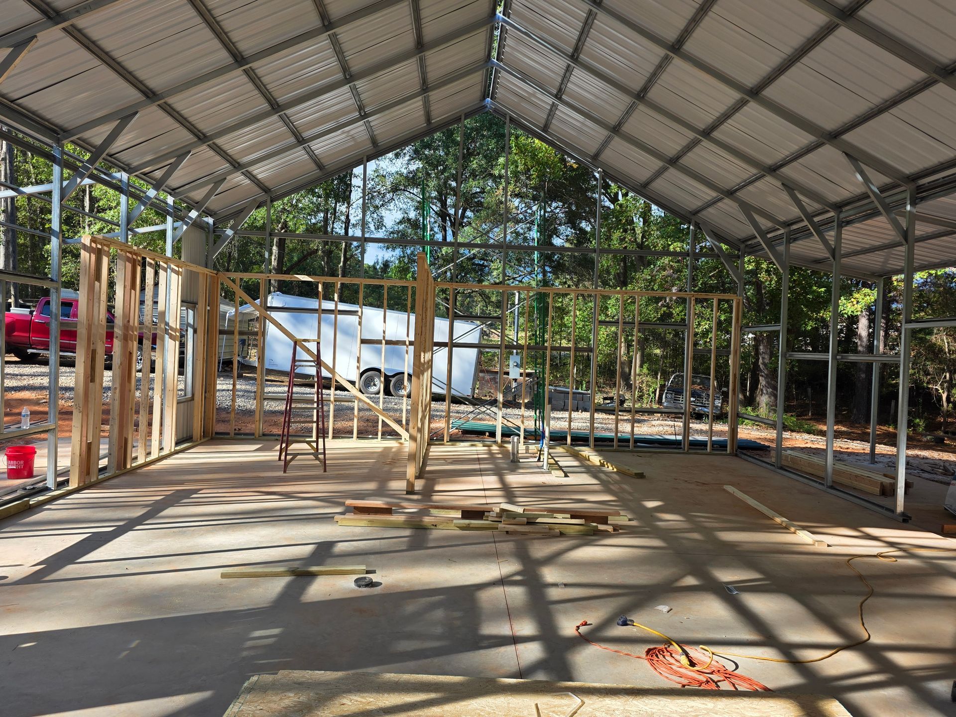 Steel frame construction, interior view with wooden wall studs. Concrete floor, metal roof. Outdoors, daytime.